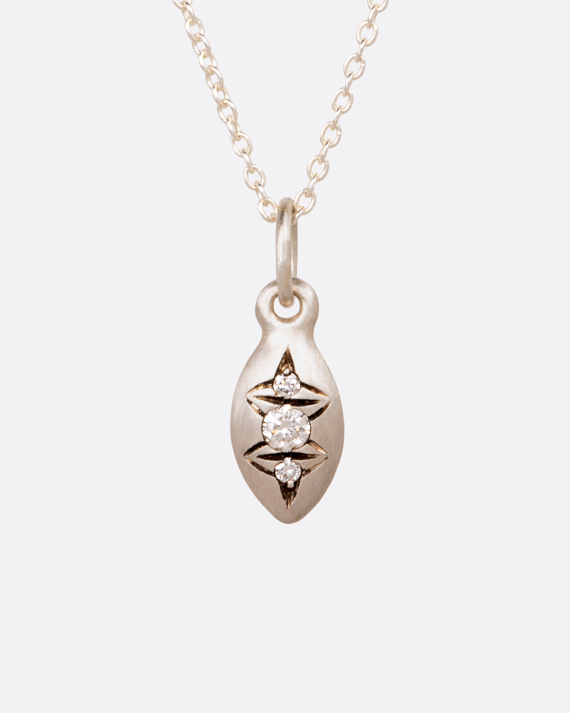 A silver cable chain necklace with a seed shaped pendant with three diamonds and oxidized etching. Shown from the front.