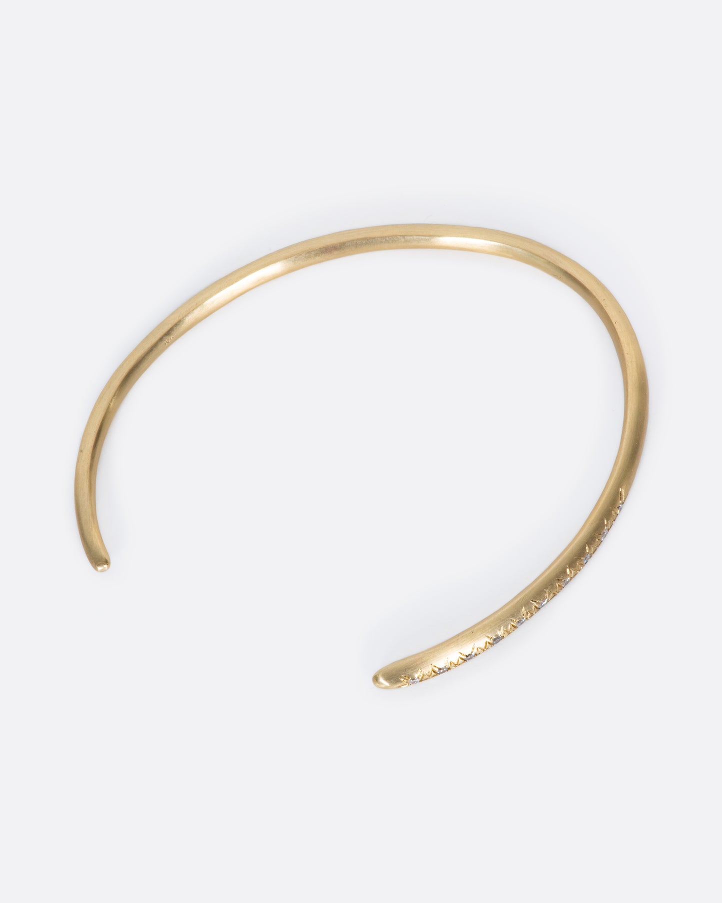 This brushed gold cuff bracelet tapers at one end and is dotted with ten light gray diamonds at the other.