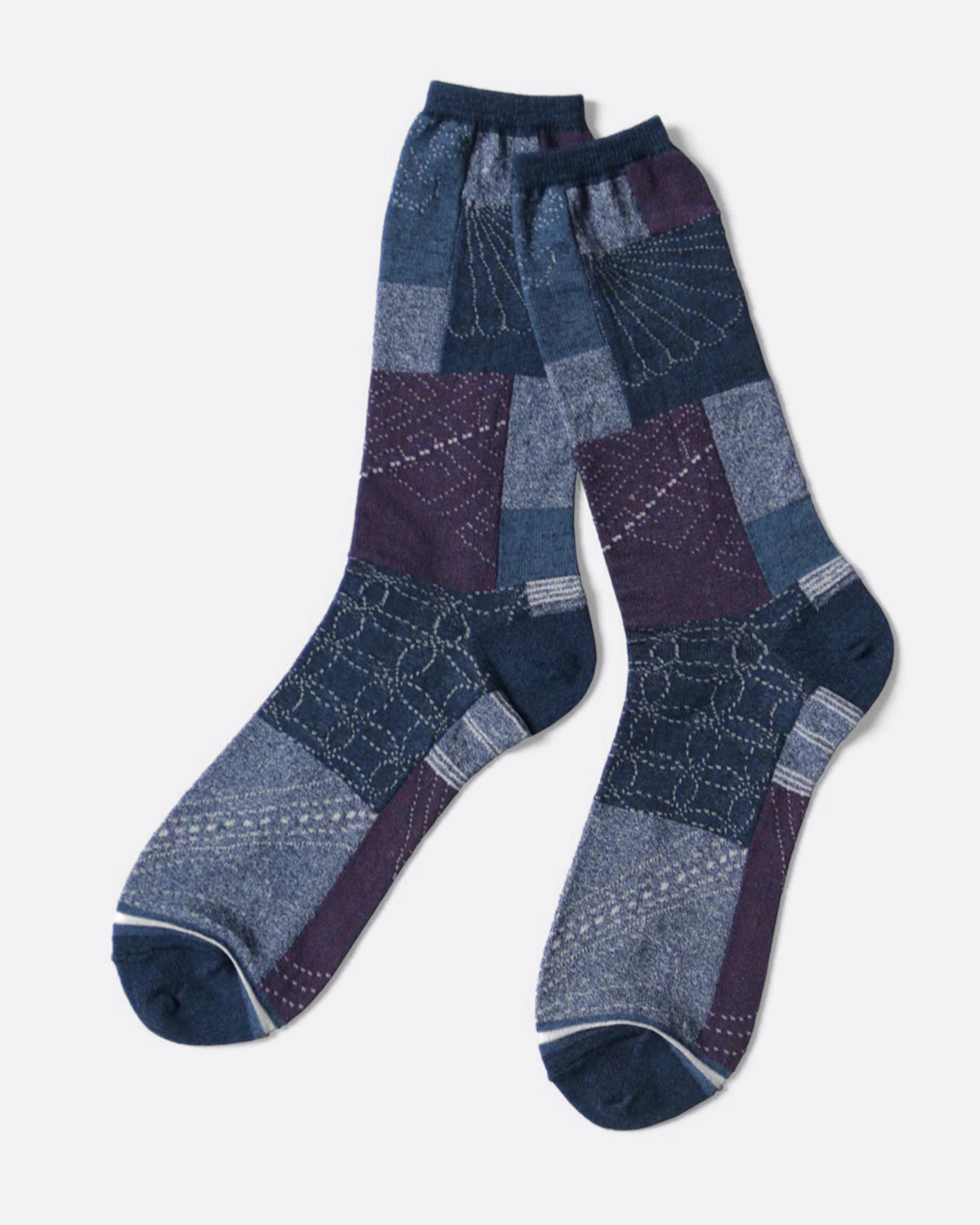 A pair of blue socks with an all- over patchwork motif. Shown lying flat from the side.