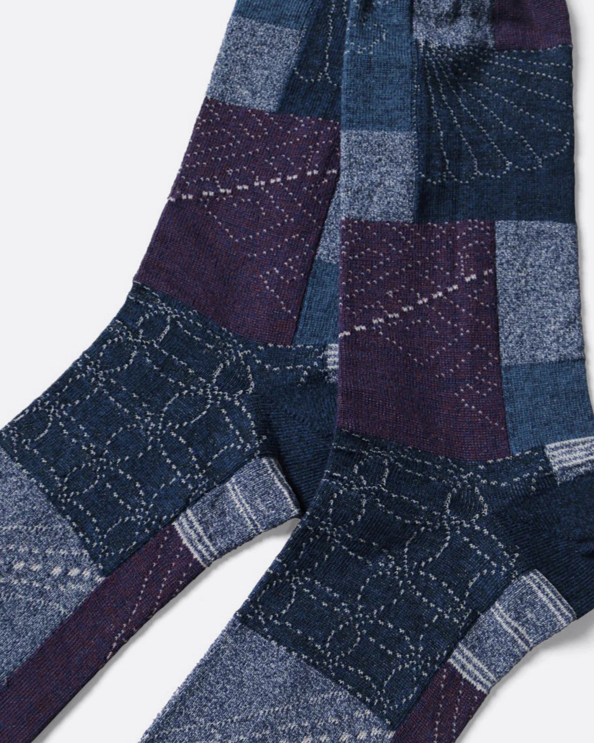 A close up of a pair of blue socks with an all- over patchwork motif. Shown lying flat from the side.