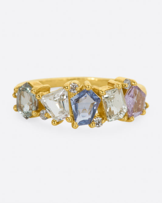 A yellow gold ring with five multicolored, mixed cut sapphires across the top, dotted with diamonds.