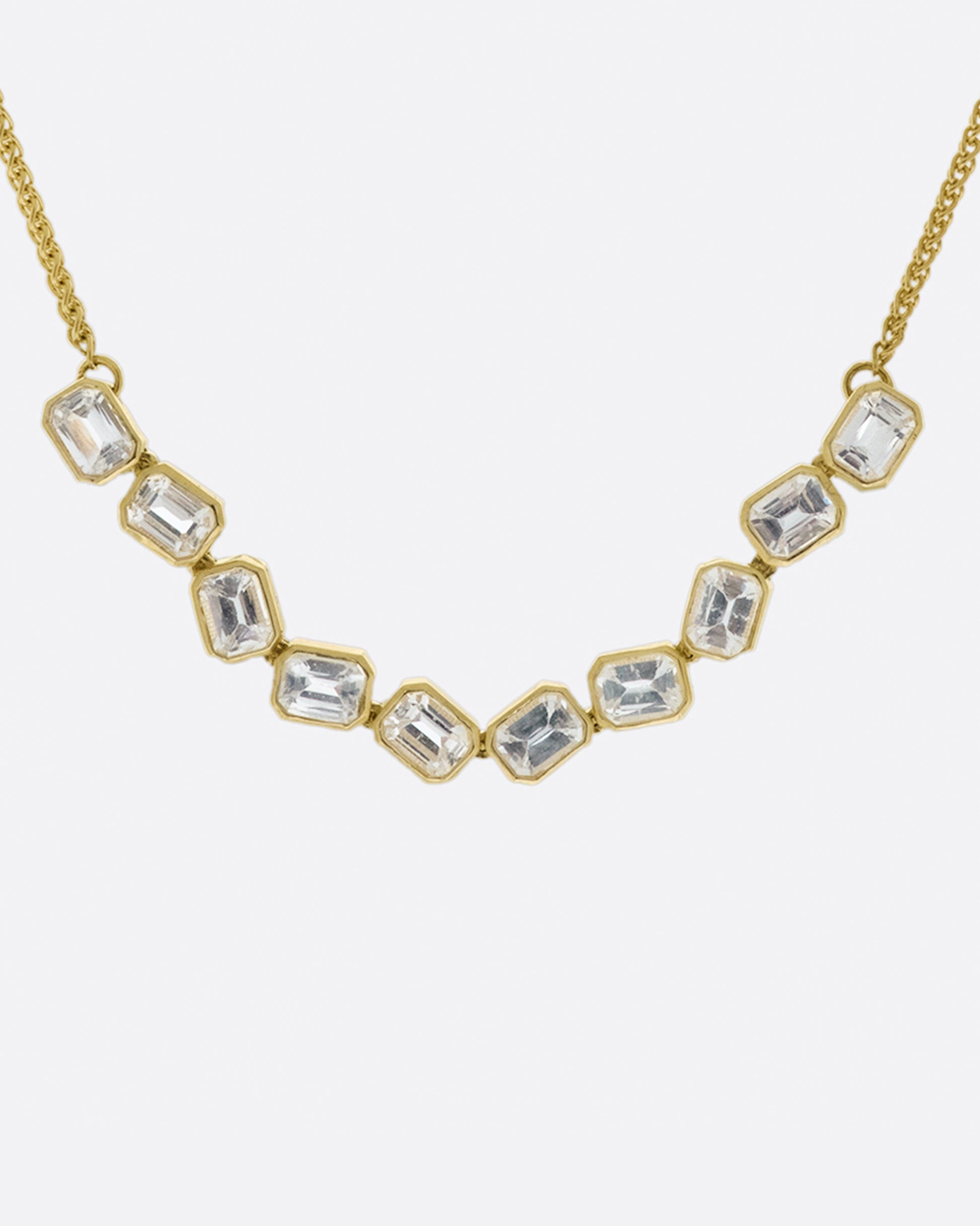 A chain necklace with a section of ten bezel set, emerald cut, white sapphires each connected to its neighbor by a hinge so the whole piece moves fluidly.