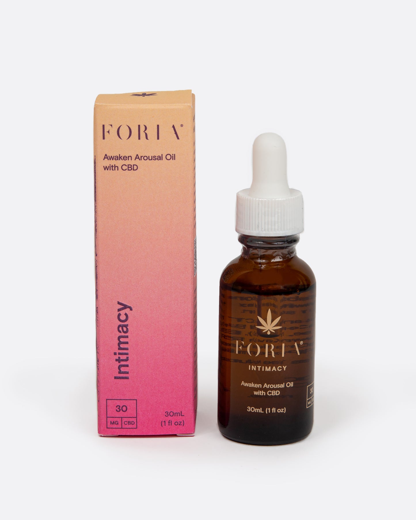 A brown glass bottle of Foria CBD Awaken Arousal Oil bottle standing next to the box. Shown from the front.