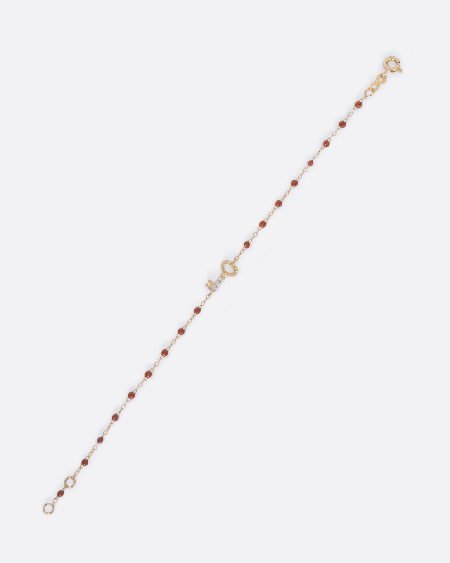 A yellow gold chain bracelet with copper resin drops and a key, lined in diamonds.