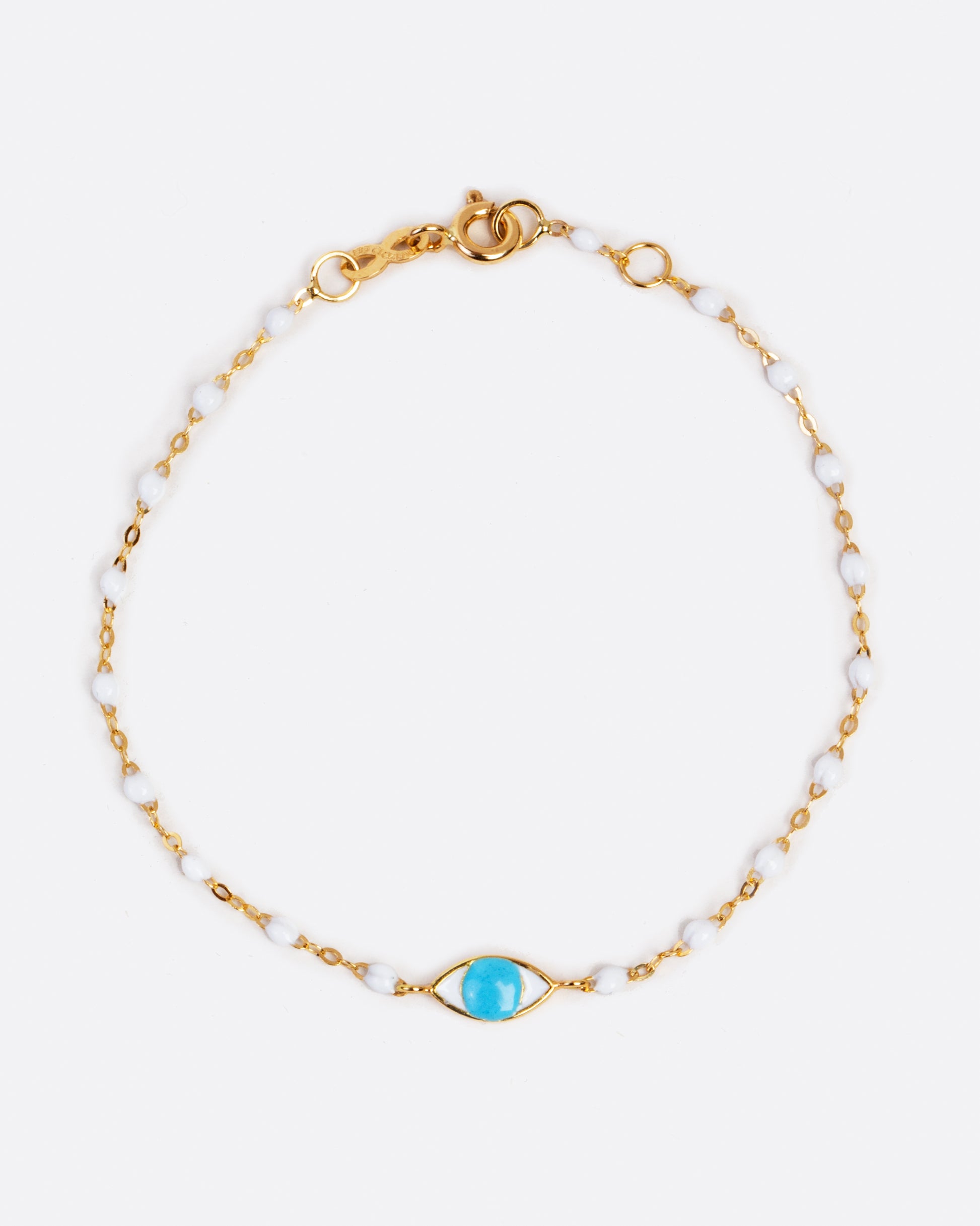 Yellow gold bracelet dipped in white resin, to create a beaded effect. In the middle is an eye charm with a blue resin iris.