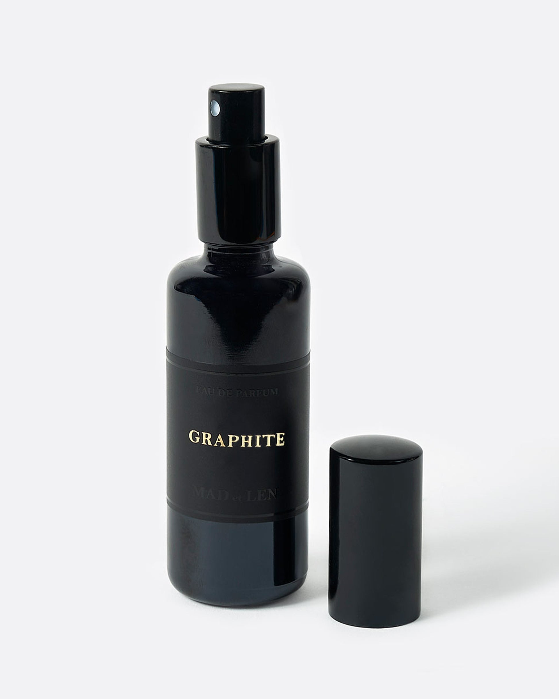 A black perfume bottle with a spray top and GRAPHITE in gold letters on its black label. A black cap sits next to it. Shown from the front.