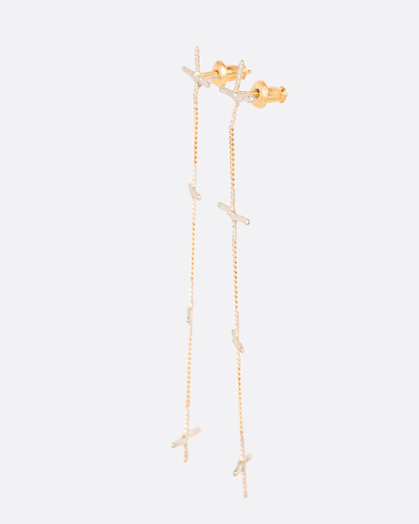 A pair of long earrings with four silver crosses and yellow gold chain in an alternating pattern. Shown from the side.