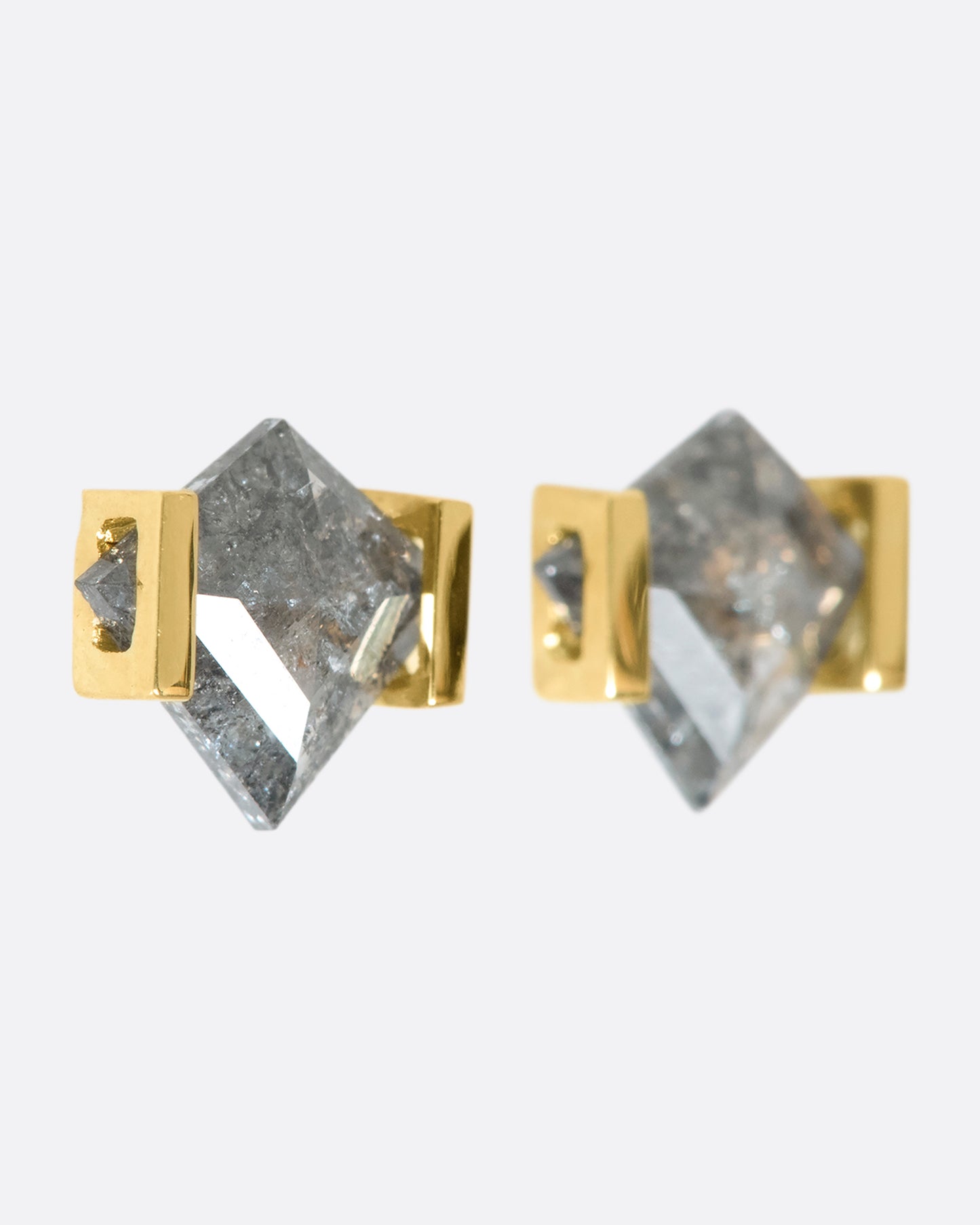 A close up of a pair of kite shaped grey diamonds in delicate gold settings.