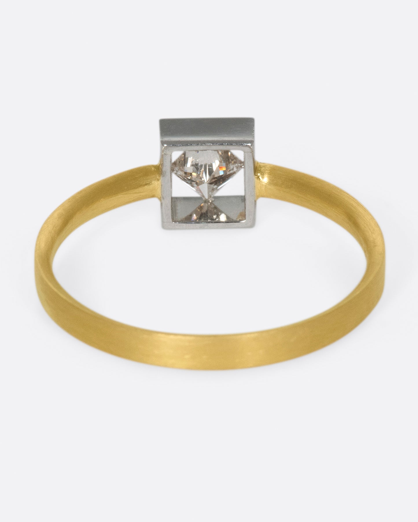 A geometric solitaire ring with a princess cut diamond set on its side in a platinum setting on a yellow gold band.