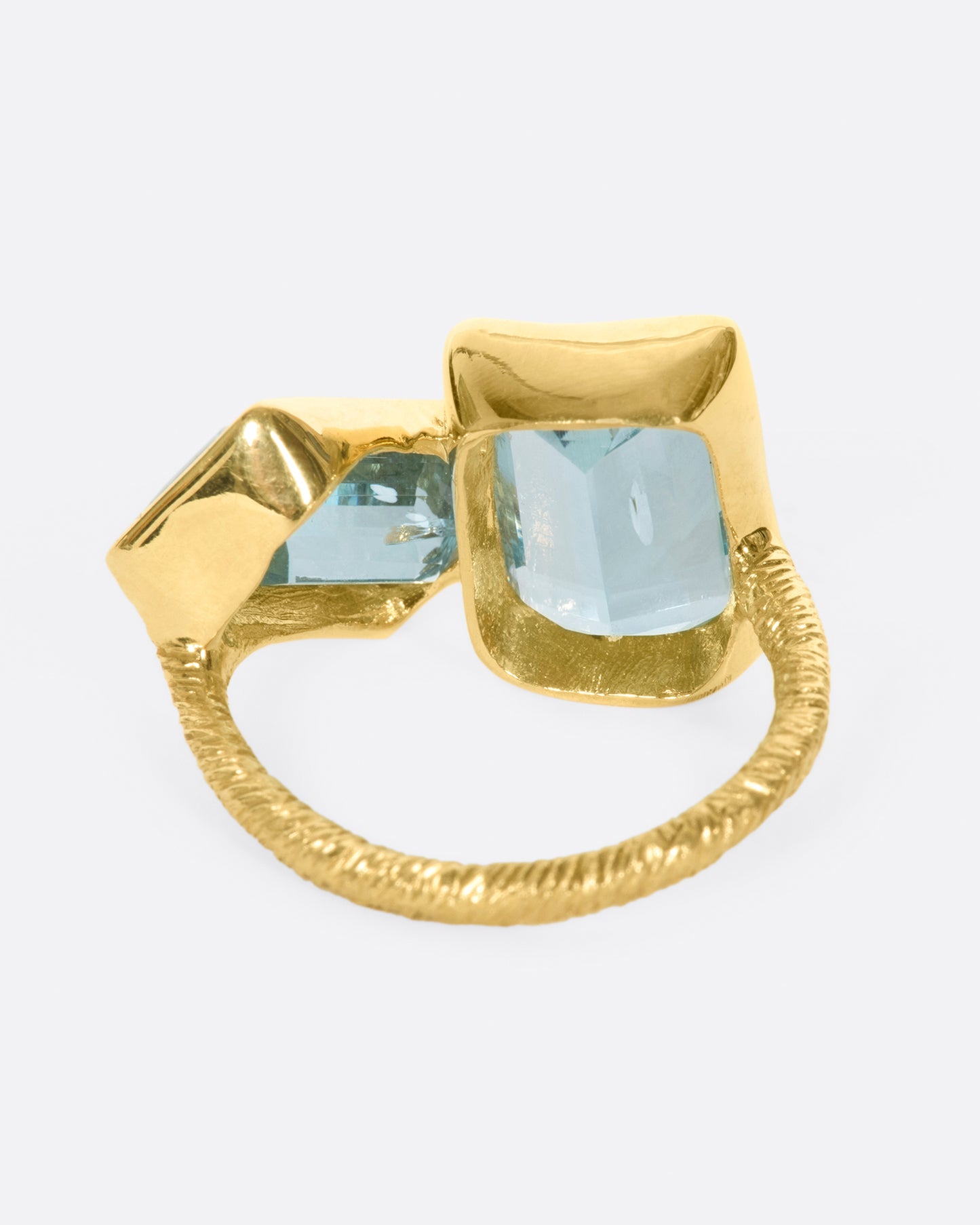 A yellow gold ring featuring two large emerald cut aquamarines set slightly askew