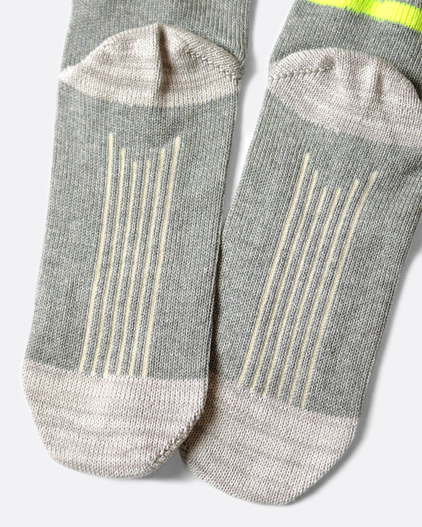 A pair of light gray socks that hit mid-ankle with an Ortega pattern across the top of the foot in shades of brown, and a neon green band at the top.