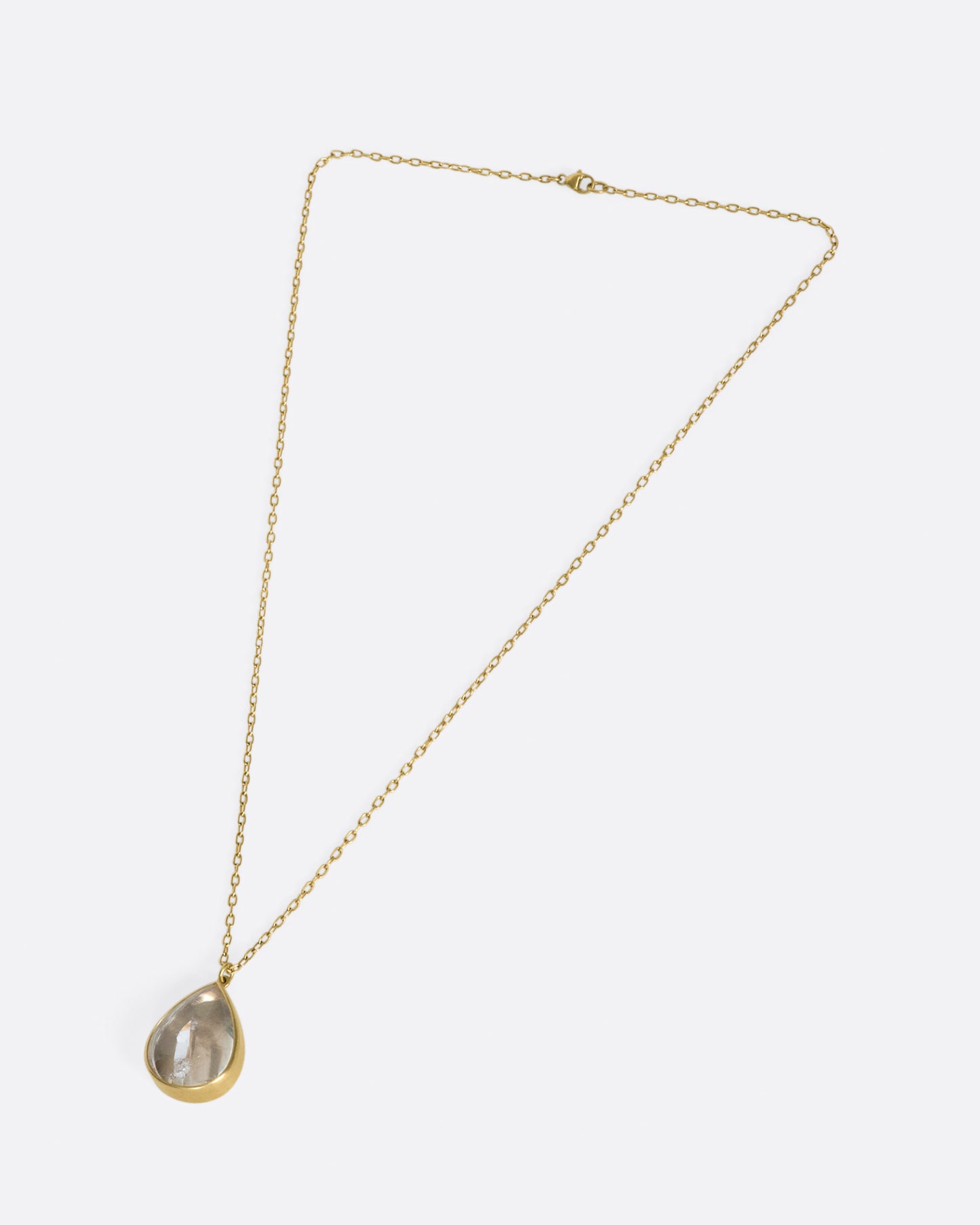 A gold necklace with a quartz crystal teardrop pendant.