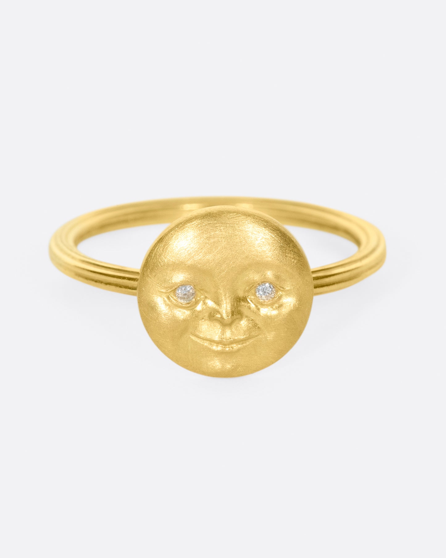 A yellow gold ring with a round moon face with diamond eyes. Shown from the front.
