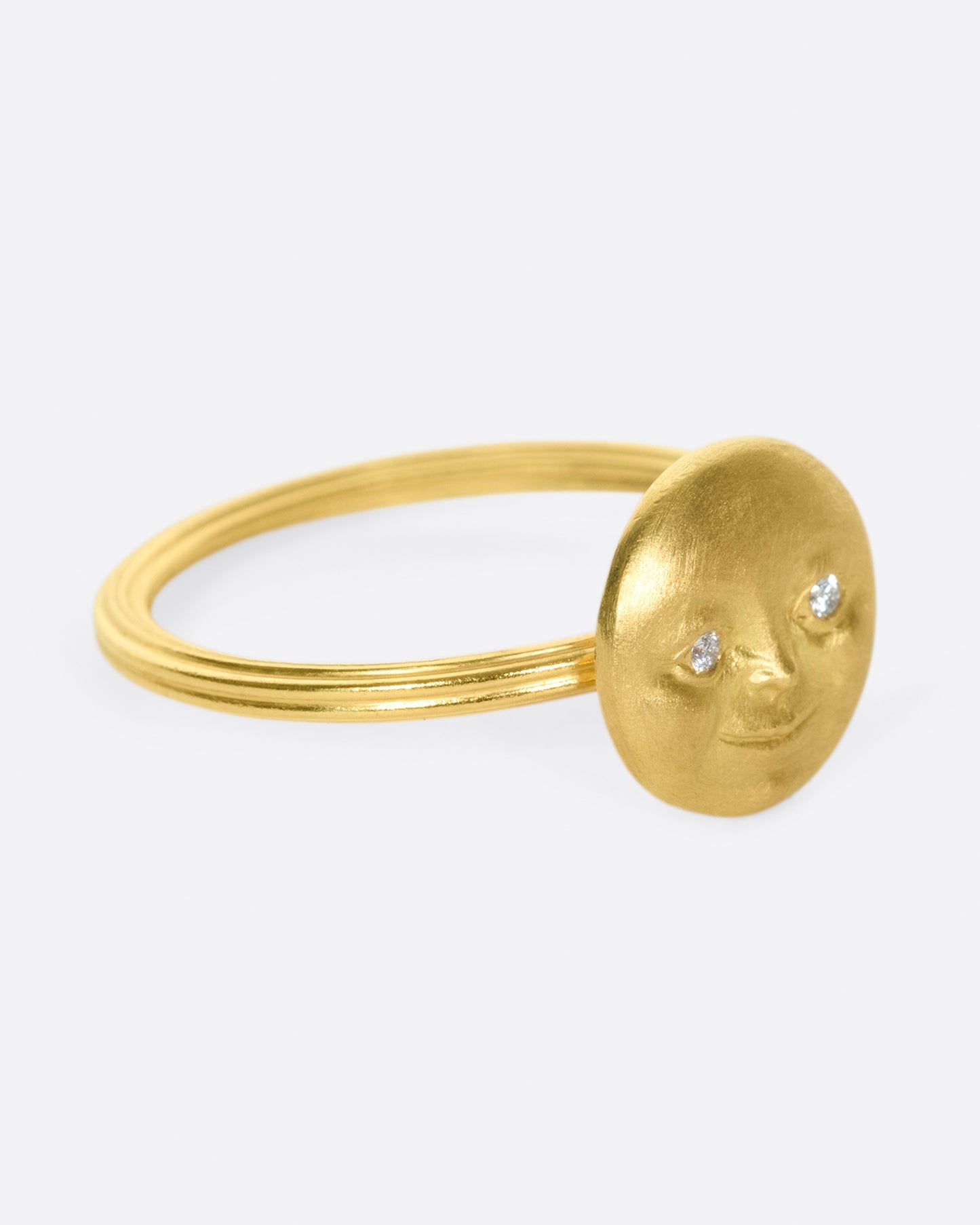 A yellow gold ring with a round moon face with diamond eyes. Shown from the side.
