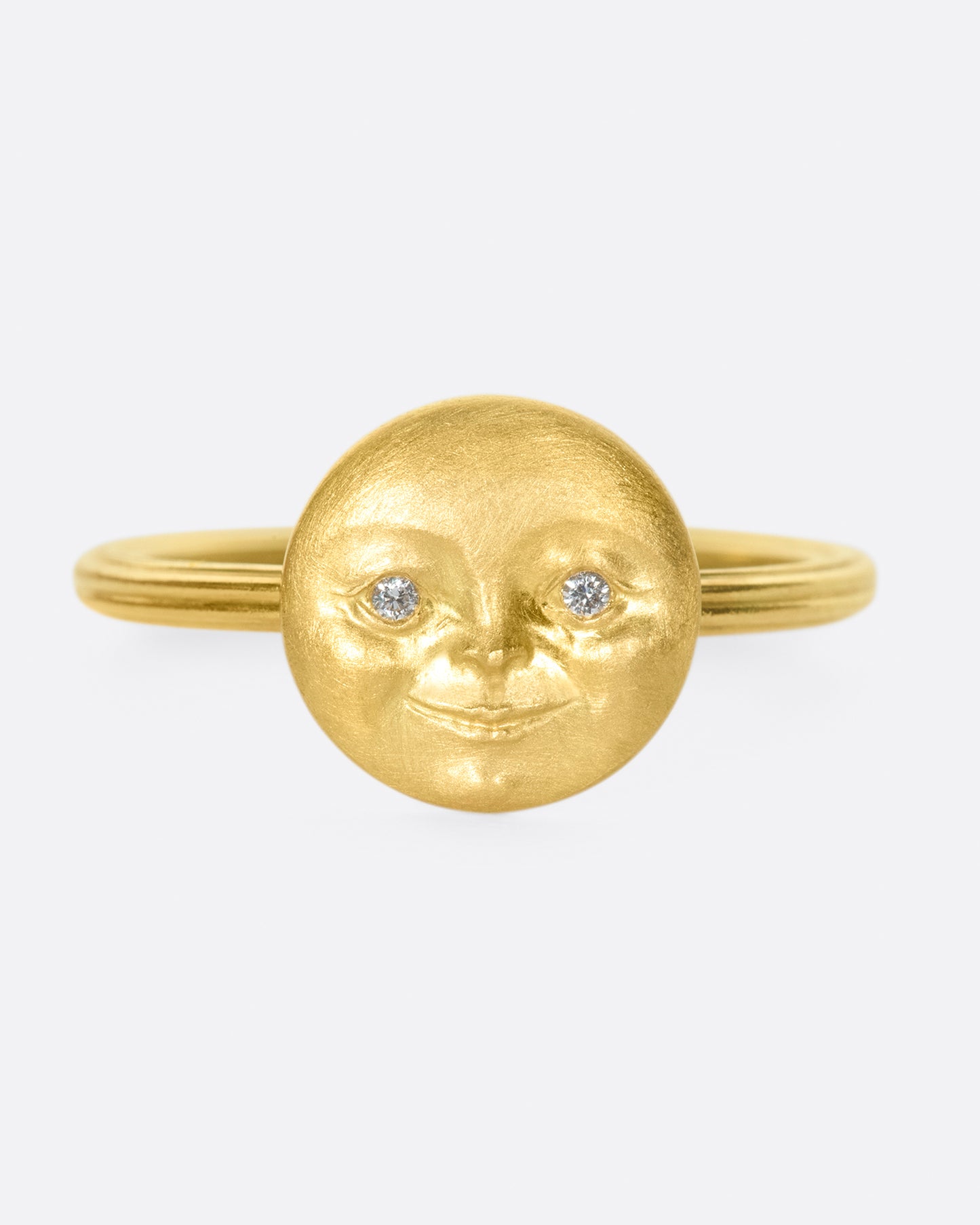 A yellow gold ring with a round moon face with diamond eyes. Shown from the front.