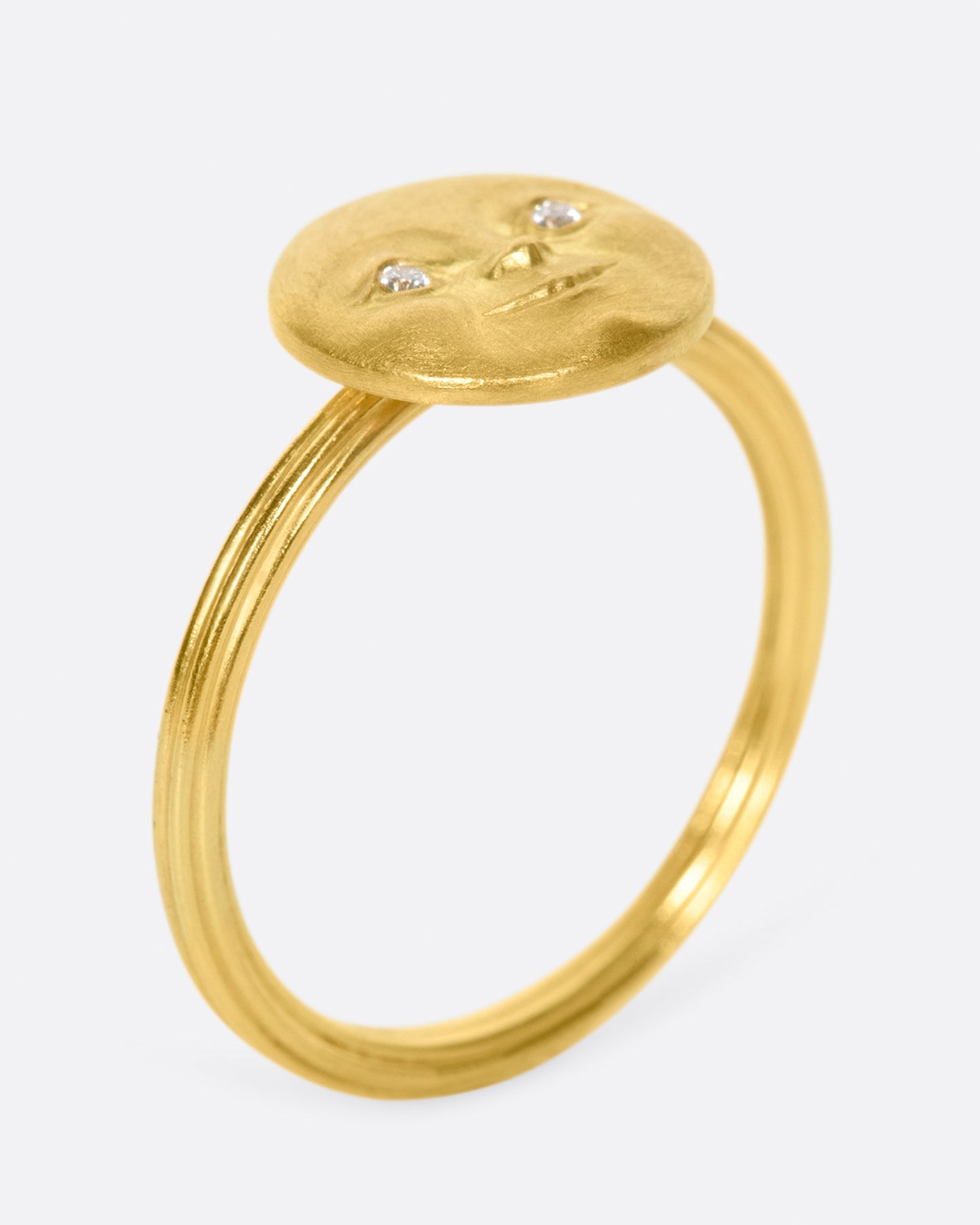 A yellow gold ring with a round moon face with diamond eyes. Shown standing up from the side.
