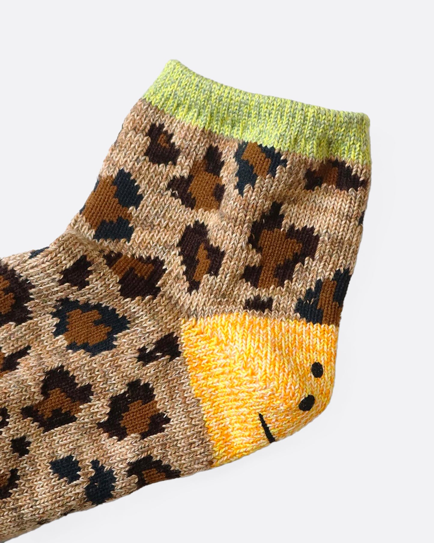 A close up of a leopard print ankle sock with a smiley face on the heel.