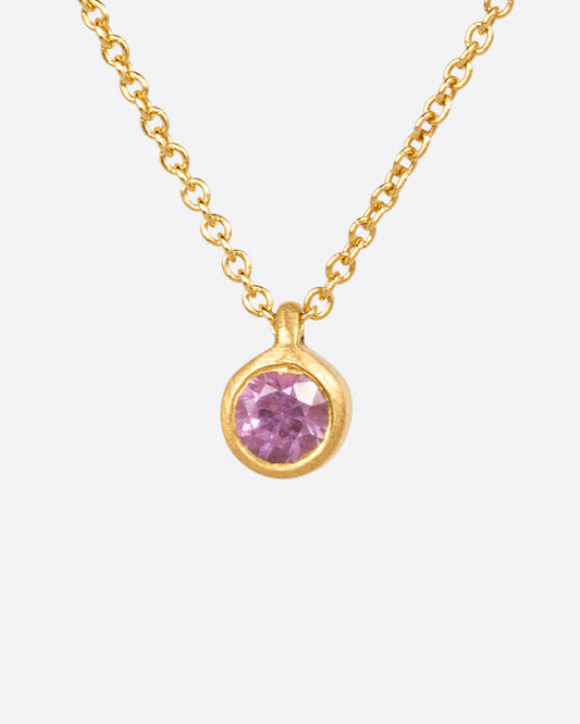 A rosy pink sapphire pendant set in a matte yellow gold bezel