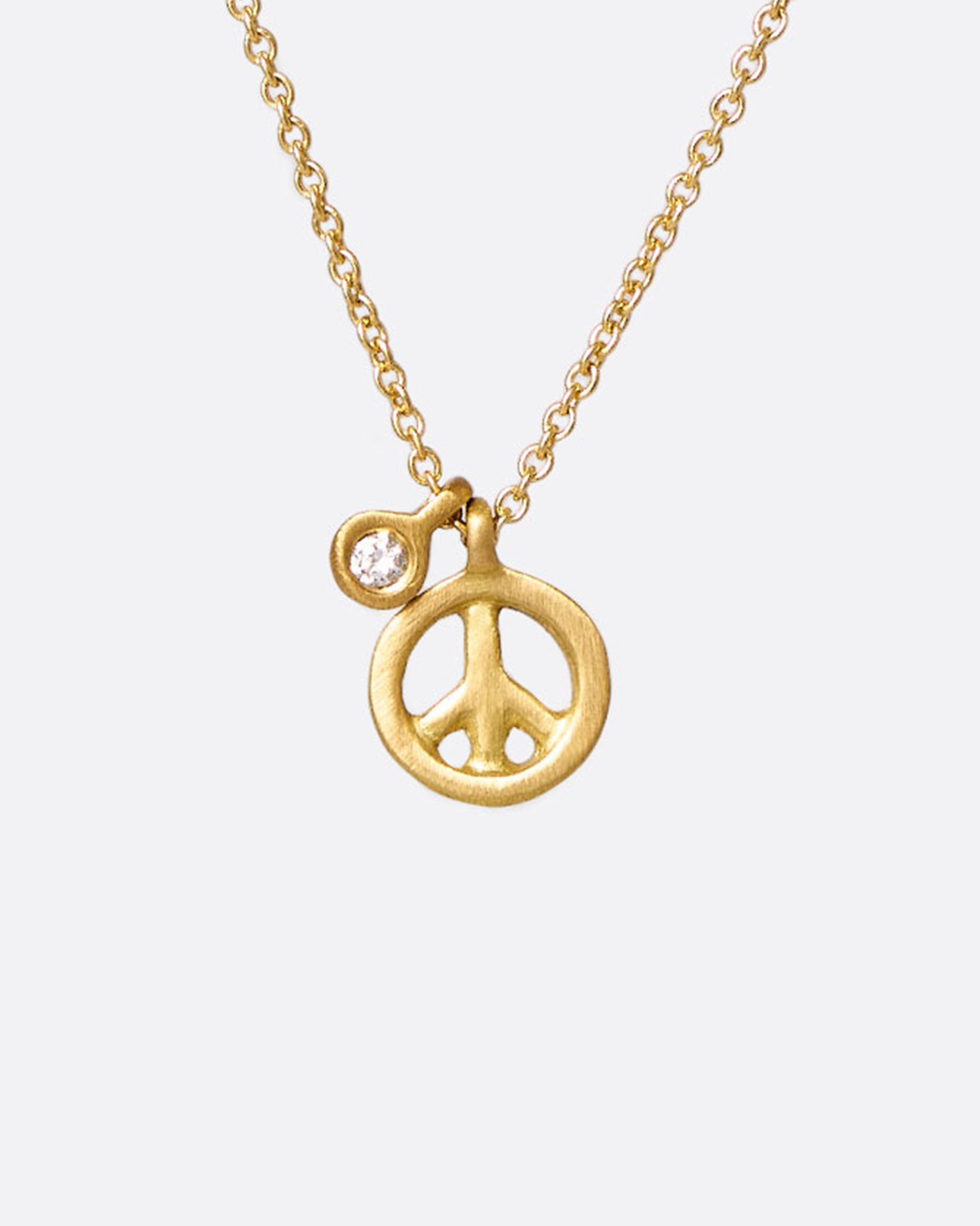 A yellow gold cable chain necklace with a peace sign pendant and a bezel set diamond tag. Shown from the front.