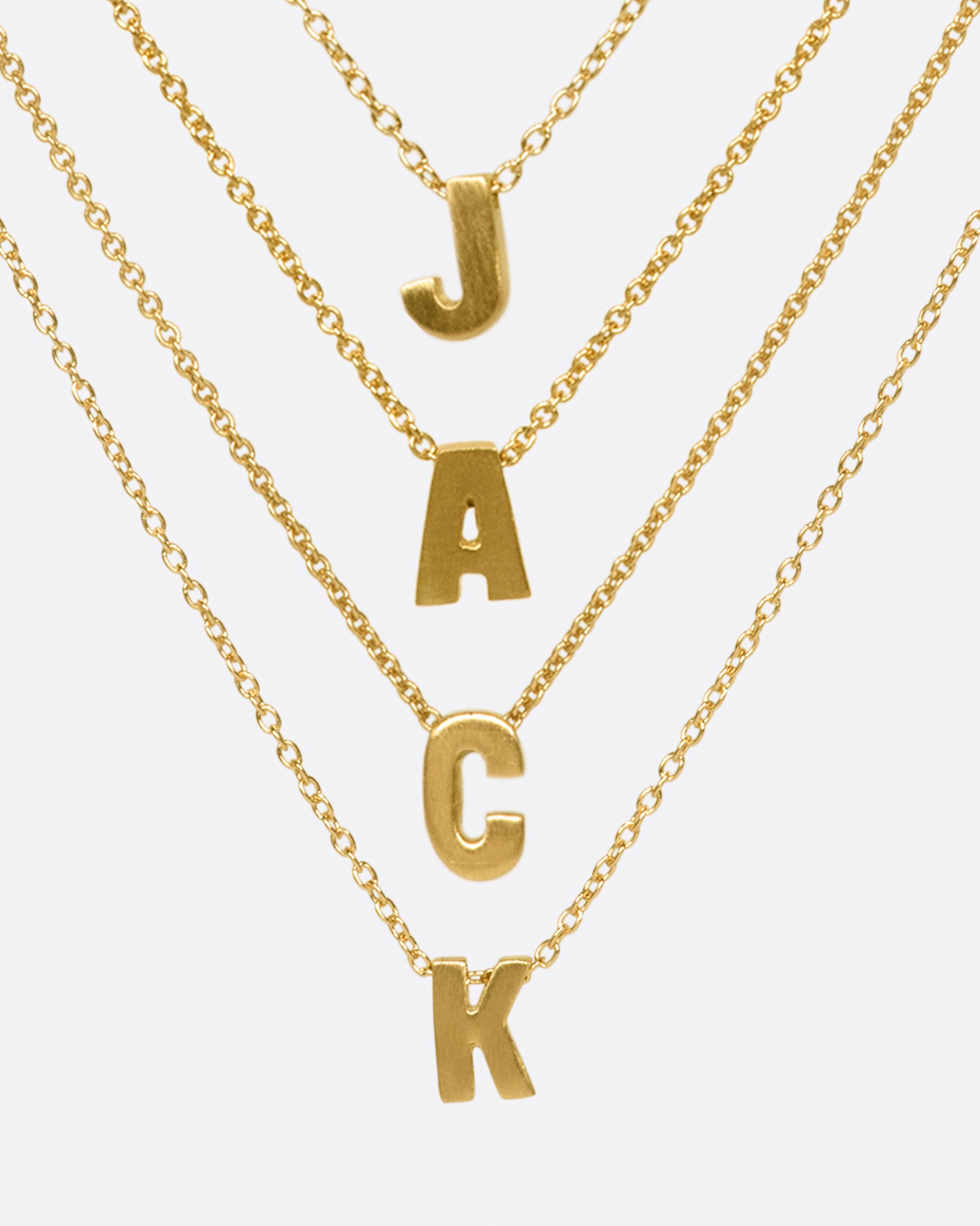 Four yellow gold cable chain necklaces with initial pendants. Shown stacked to spell 'JACK' from the front.