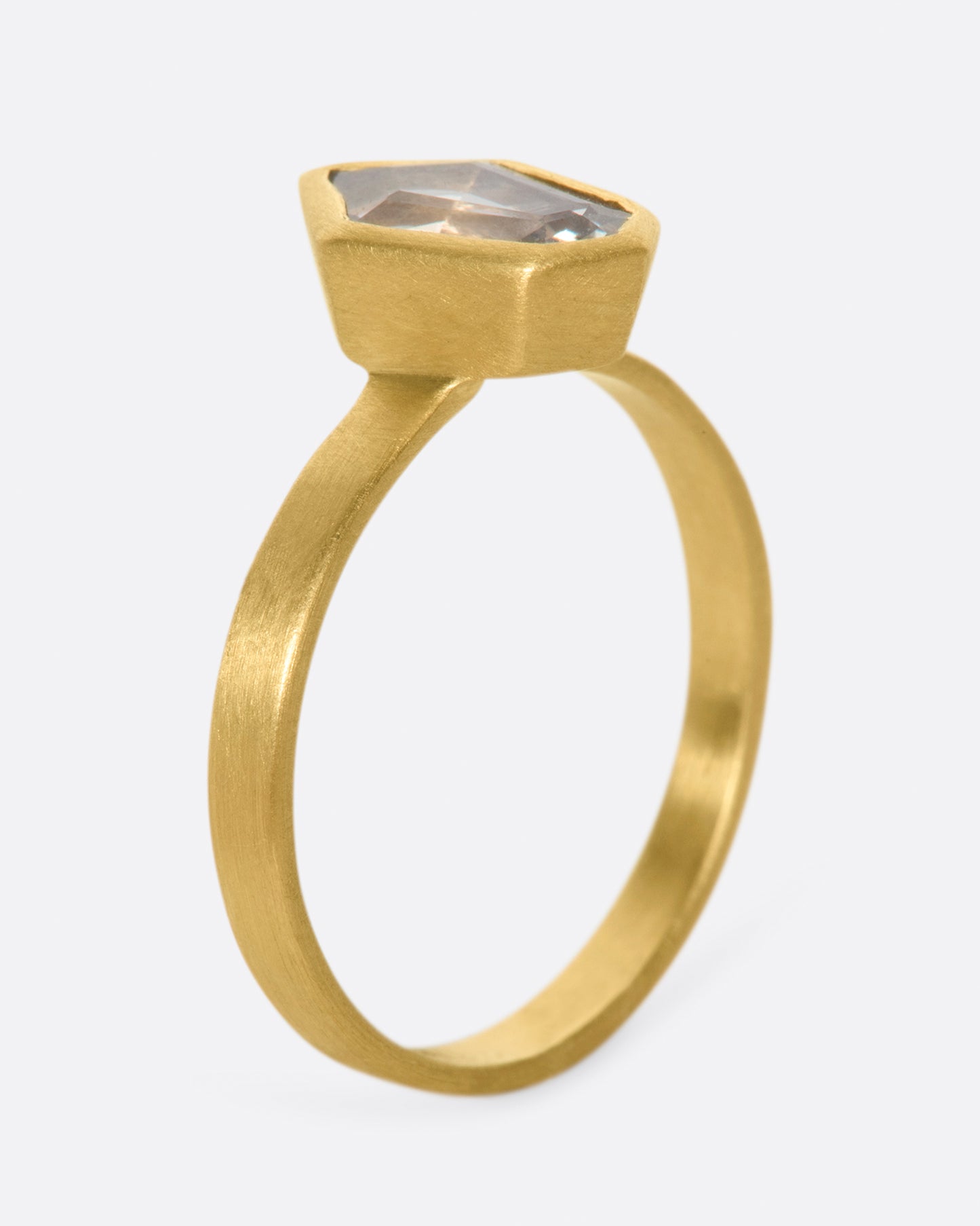 A matte gold solitaire ring with a bezel set, shield shaped sapphire.