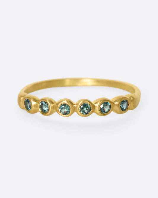 A matte gold band with teal green sapphires almost halfway around.