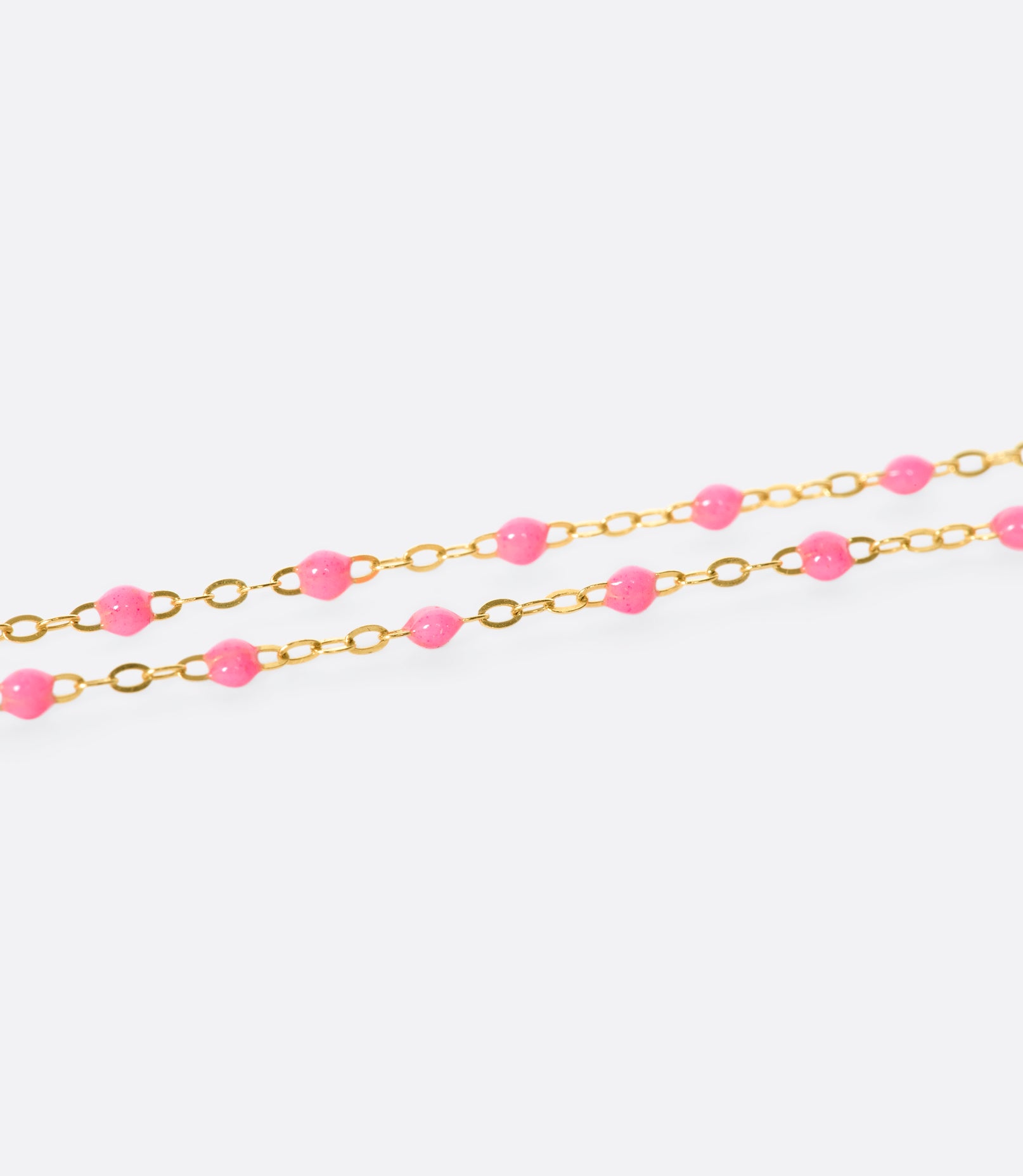 A close up view of a yellow gold cable chain bracelet with pink resin droplets.