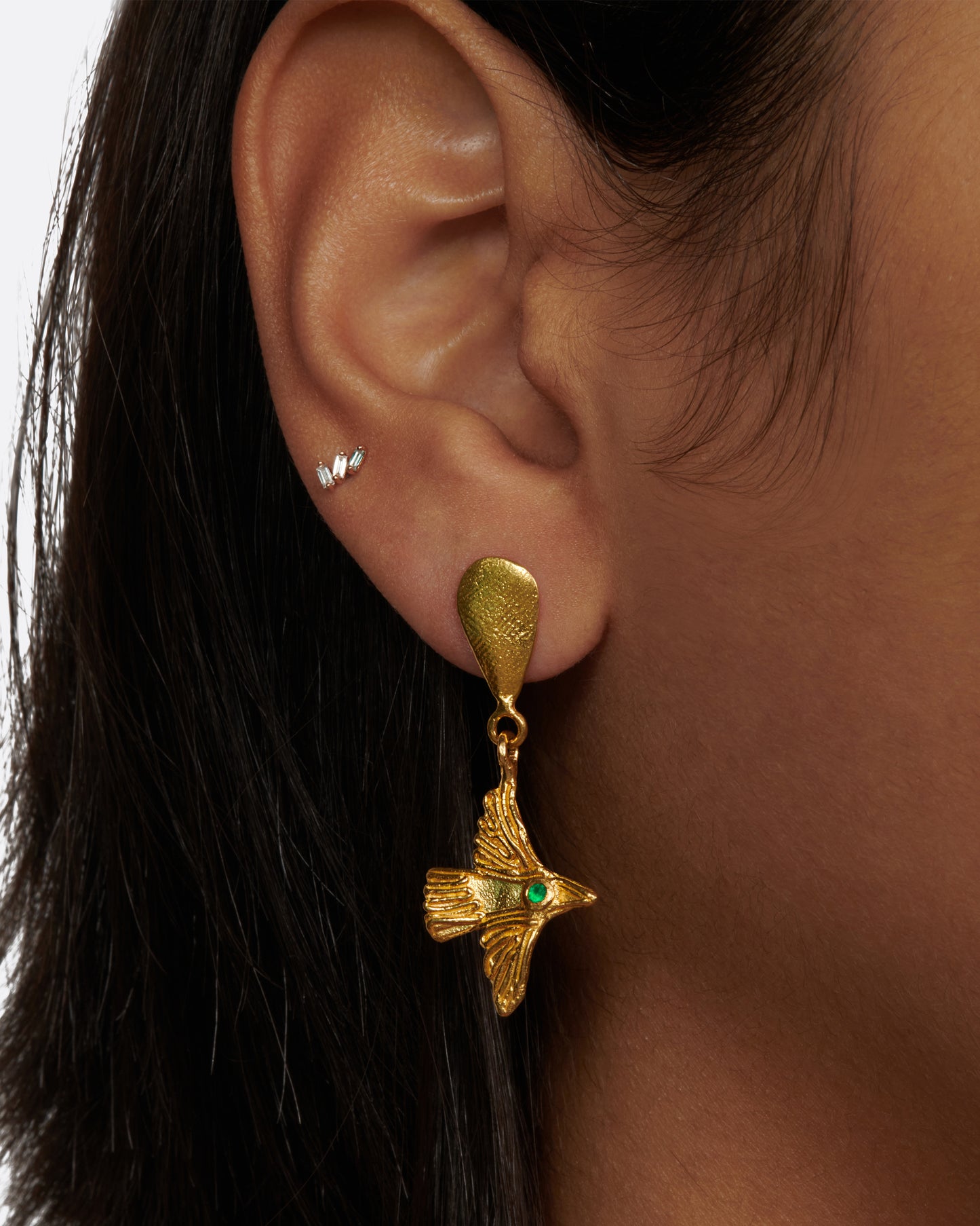 Yellow gold bird earrings with emerald eyes, a bird earring worn on an ear