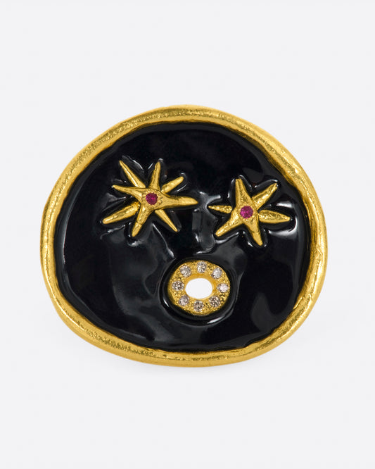 A large high karat gold ring with a round black enamel face, ruby star eyes and a open mouth covered in diamonds.