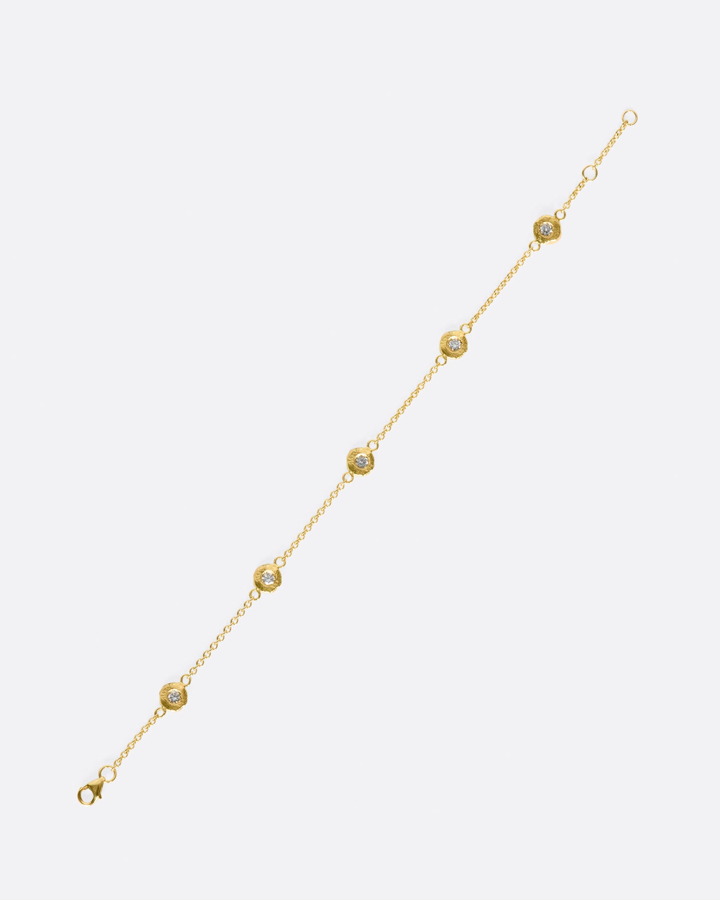 A handmade take on a classic style; this chain bracelet has five diamonds set in hand carved bezels, a bit over an inch apart.