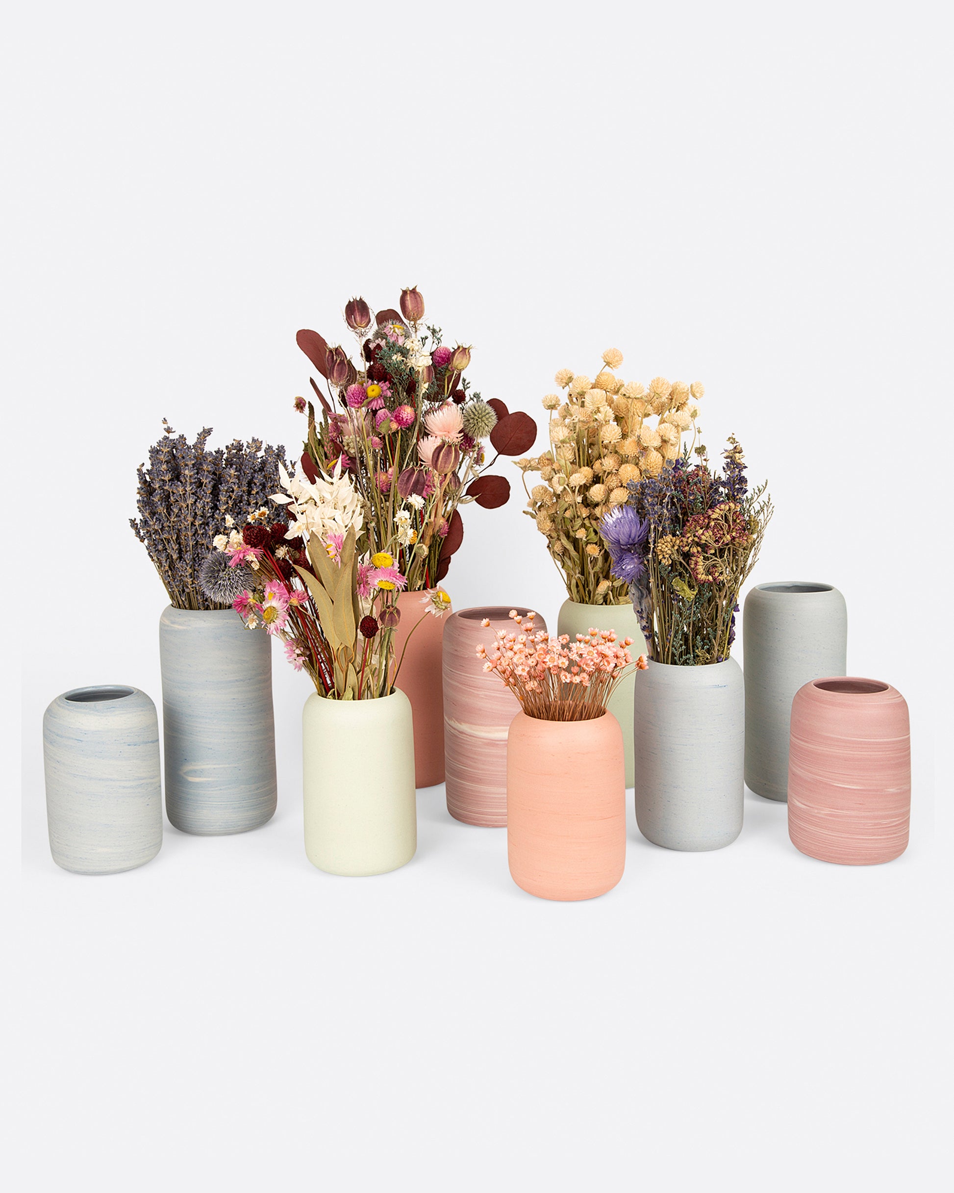 A group of all pastel colored porcelain vases, six with floral arrangements. Shown from the front.