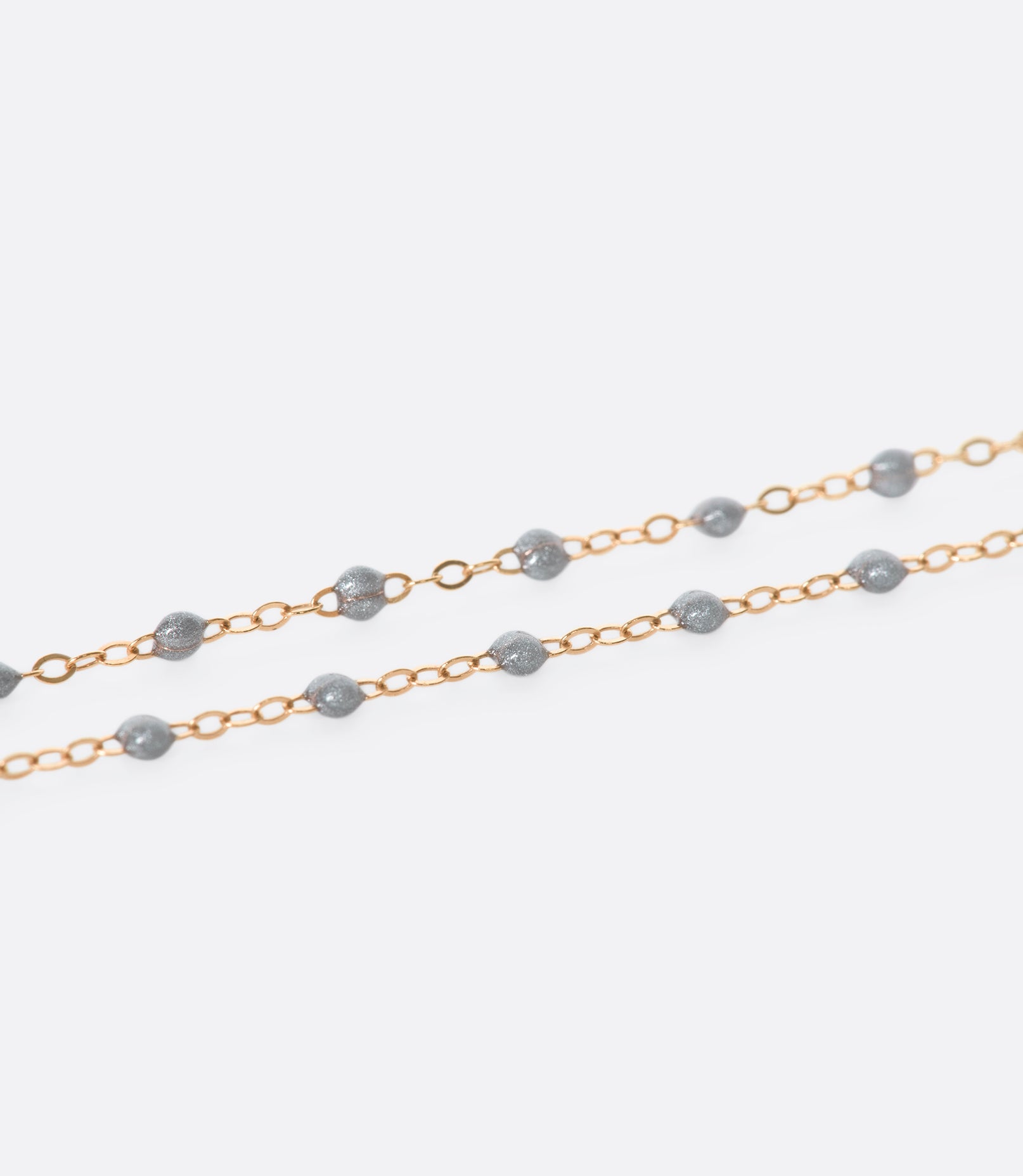 A close up view of a yellow gold cable chain bracelet with silver resin droplets.