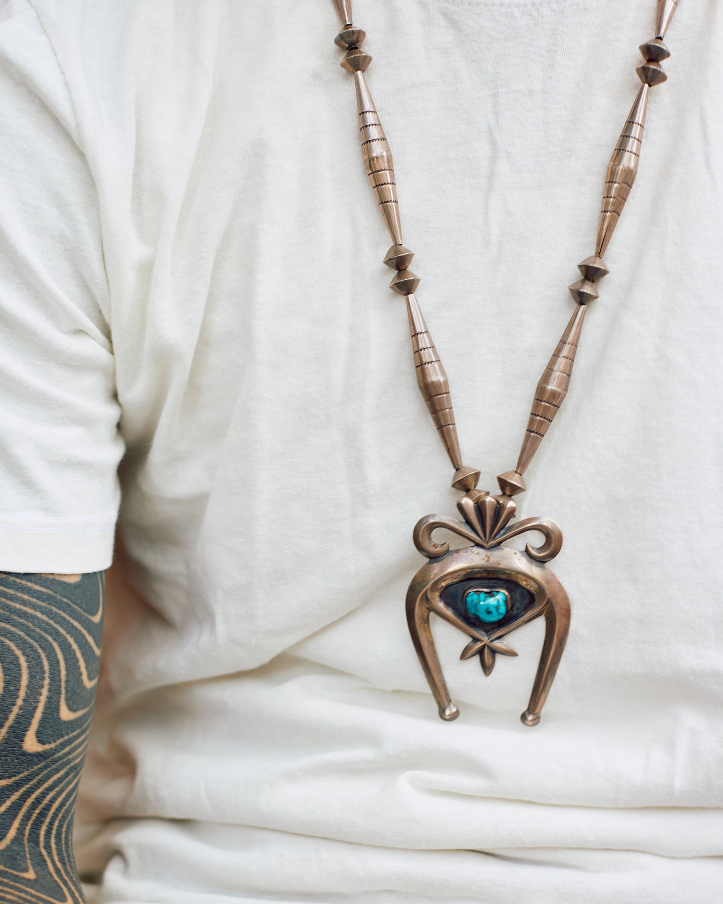 A vintage silver naja necklace with a turquoise stone at the center of the pendant, shown lying flat from the front on a person.