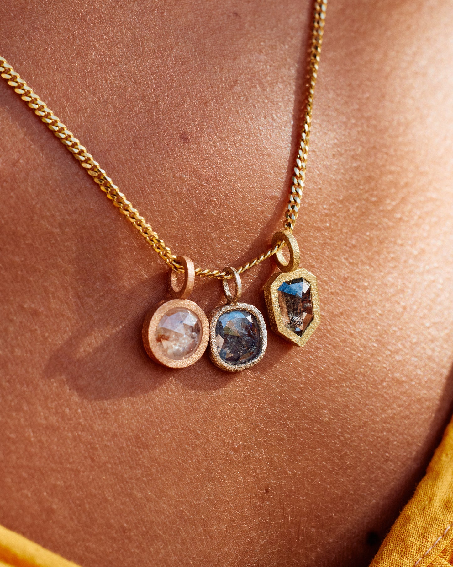 A group of three diamond pendants; one in yellow gold, one in rose gold and one in white gold, all hanging on a yellow gold chain and shown from the front on a person.