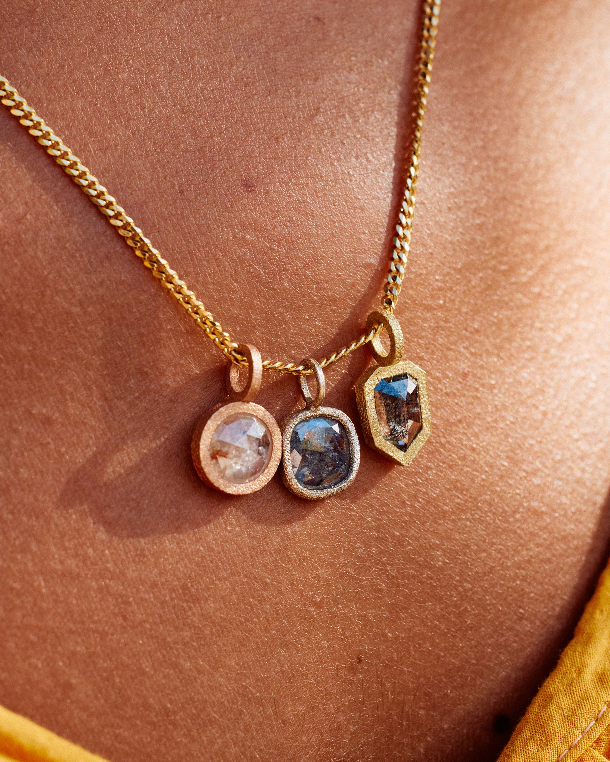 A group of three diamond pendants; one in yellow gold, one in rose gold and one in white gold, all hanging on a yellow gold chain and shown from the front on a person.