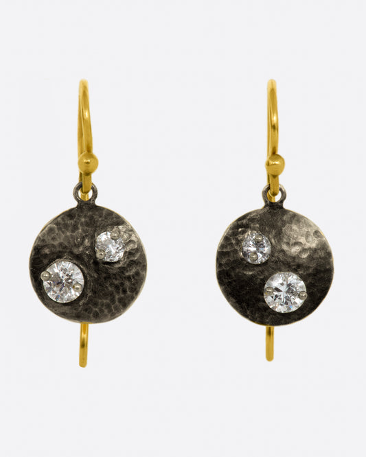 A pair of white gold hammered circle drop earrings with two round diamonds on each, yellow gold ear wires and yellow gold backsides. 