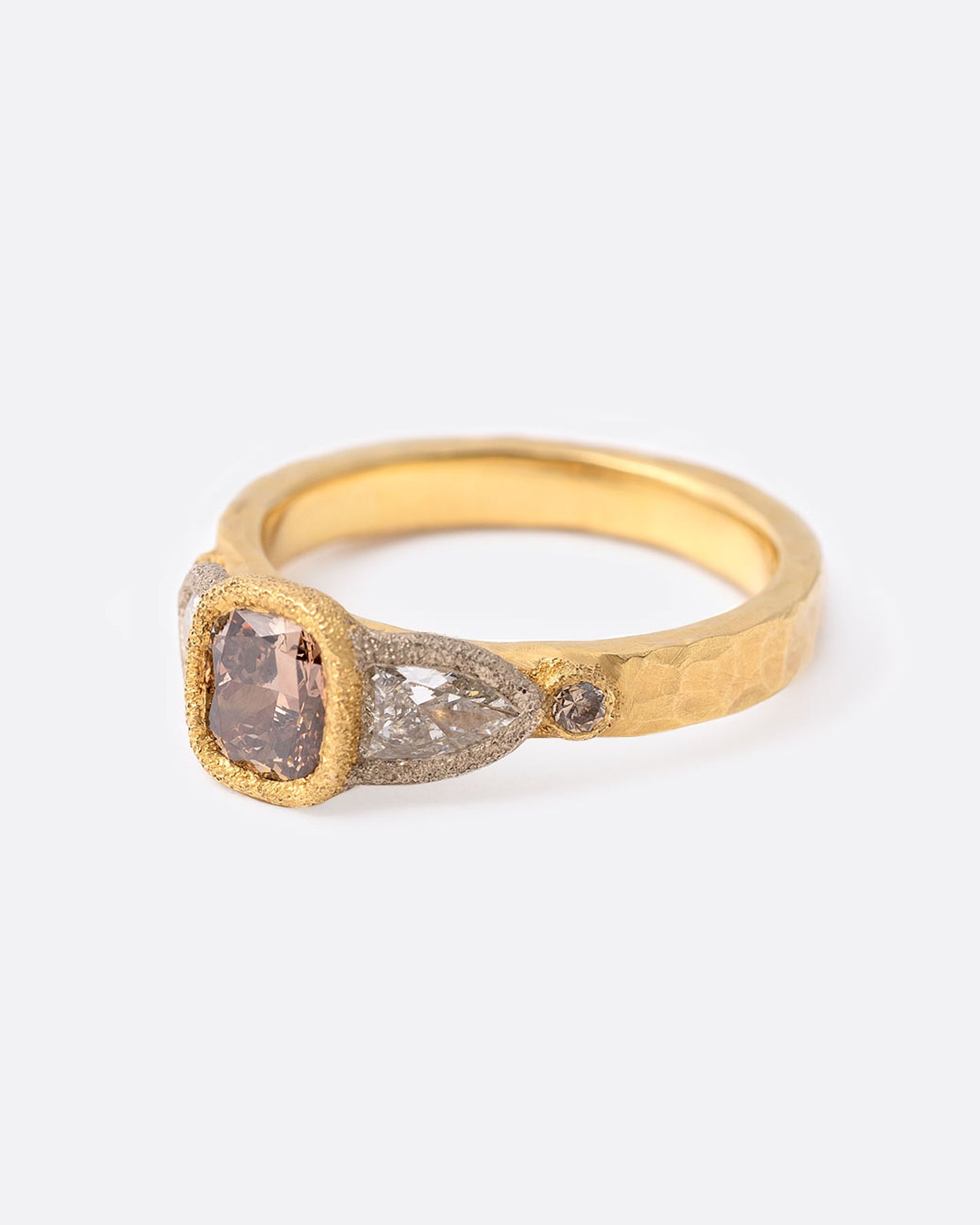 A yellow gold ring with a cushion cut cognac diamond at the center flanked by two shield cut diamonds and two smaller round cognac diamonds. Shown at an angle from the side.