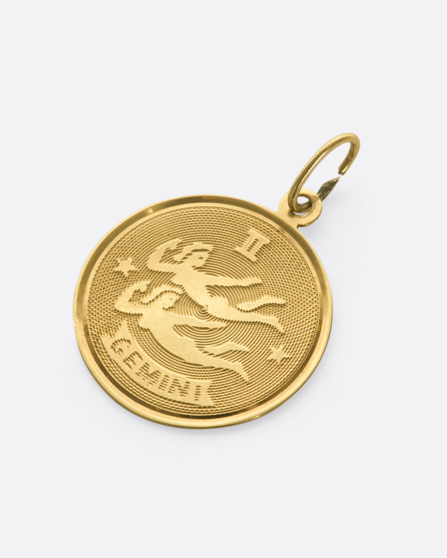 An engine turned zodiac pendant with a blank, polished backside.