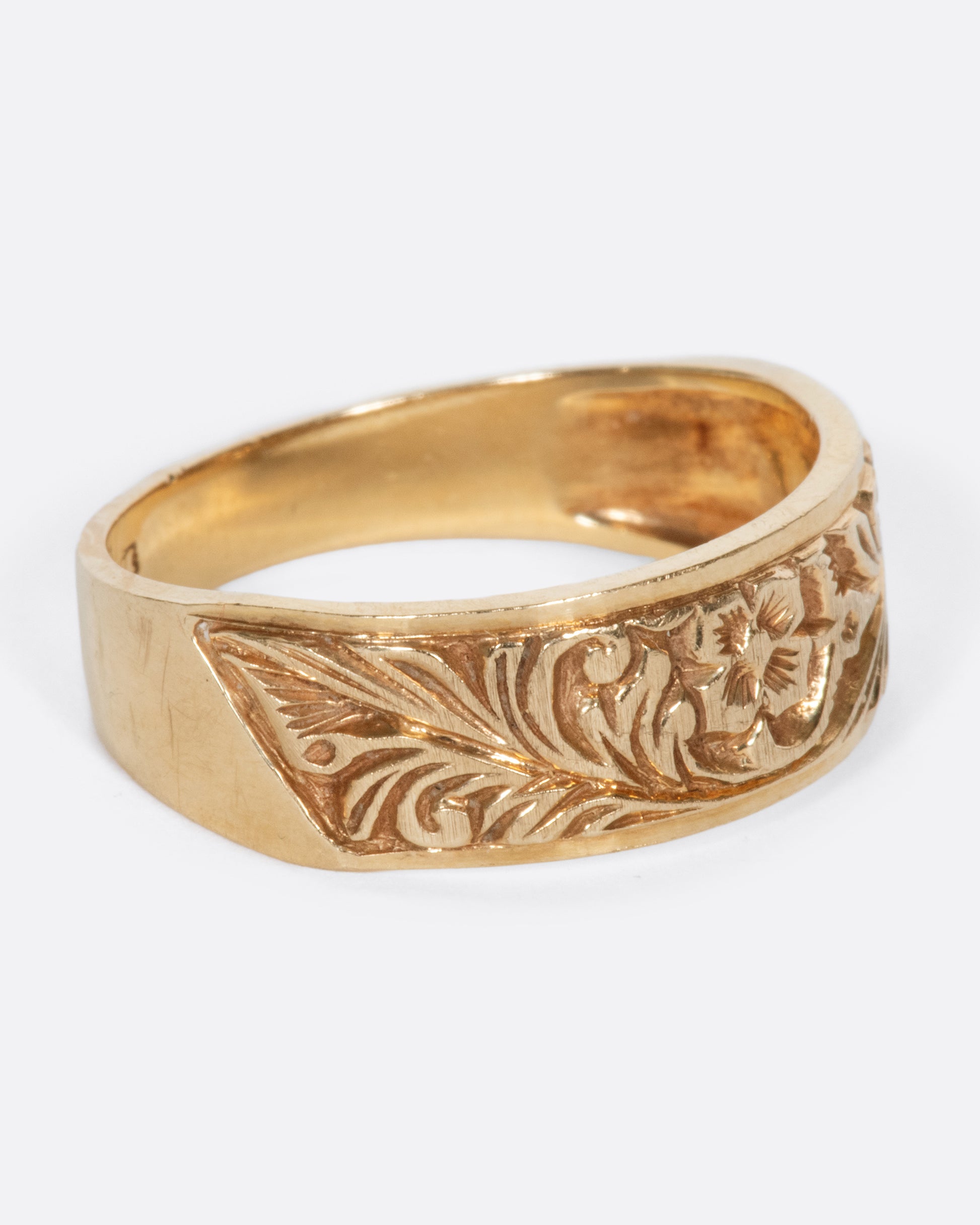A vintage yellow gold band ring with a flower and leaves carved into the front half of it.