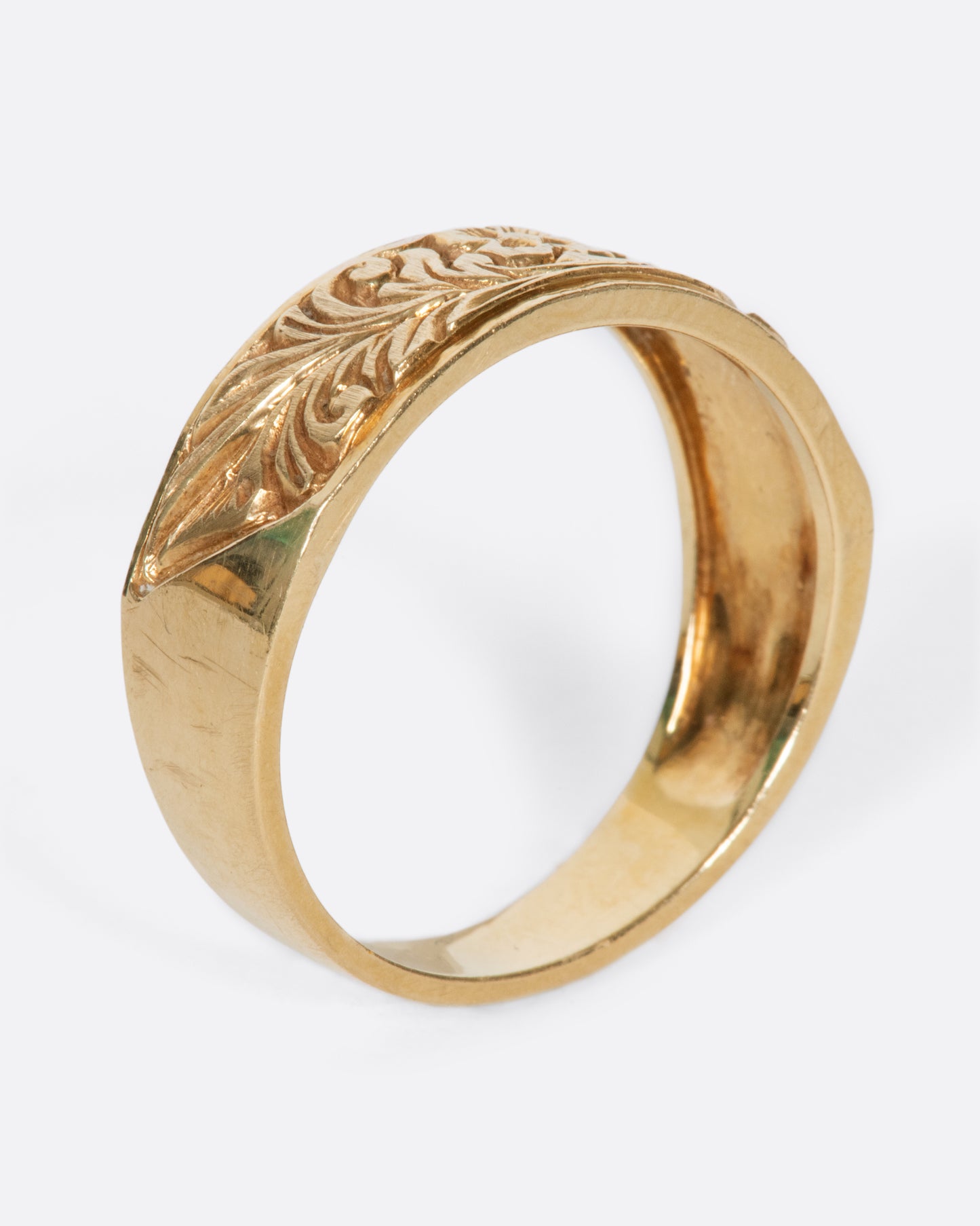 A vintage yellow gold band ring with a flower and leaves carved into the front half of it.
