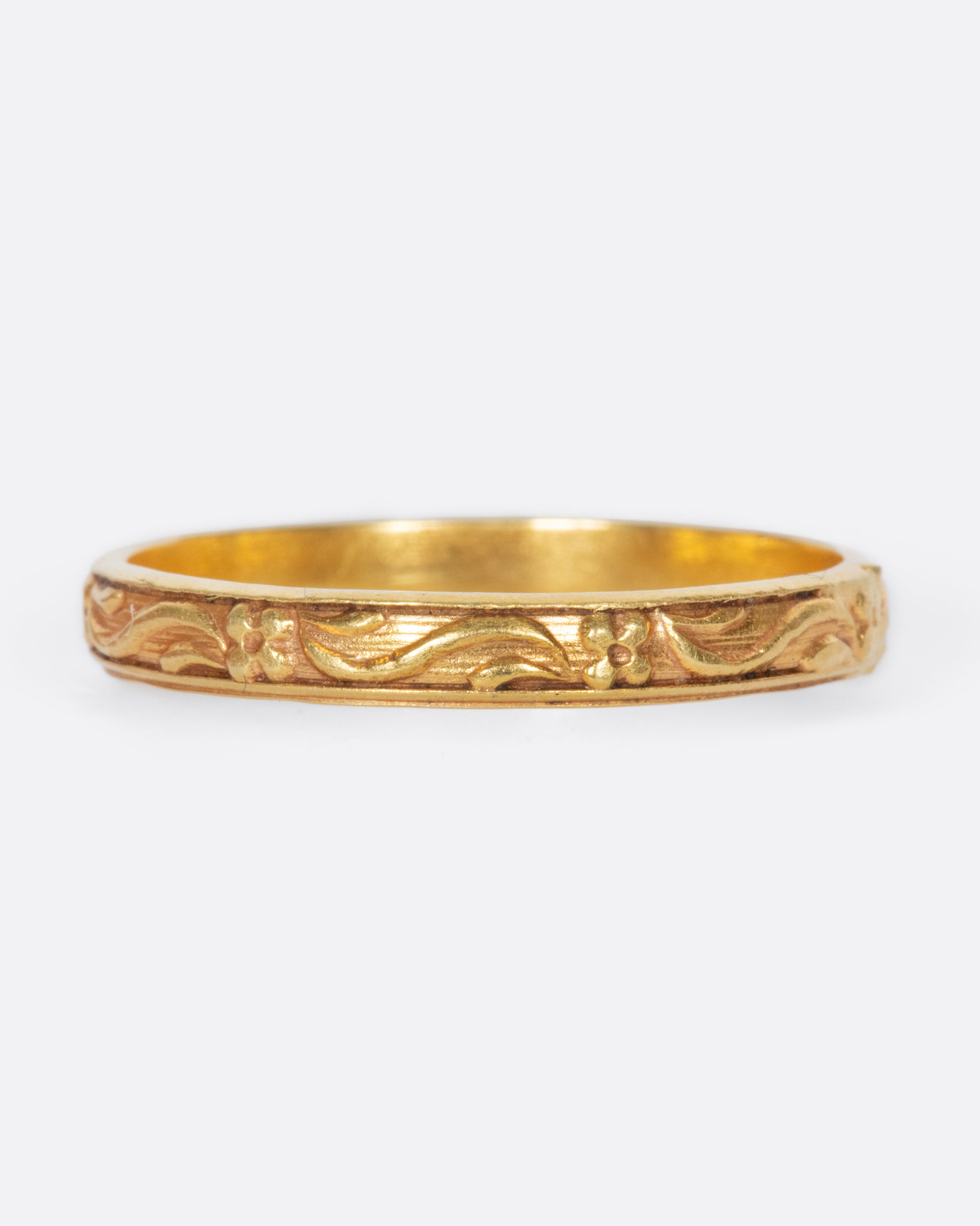 A vintage yellow gold narrow band ring with flowers and leaves throughout.