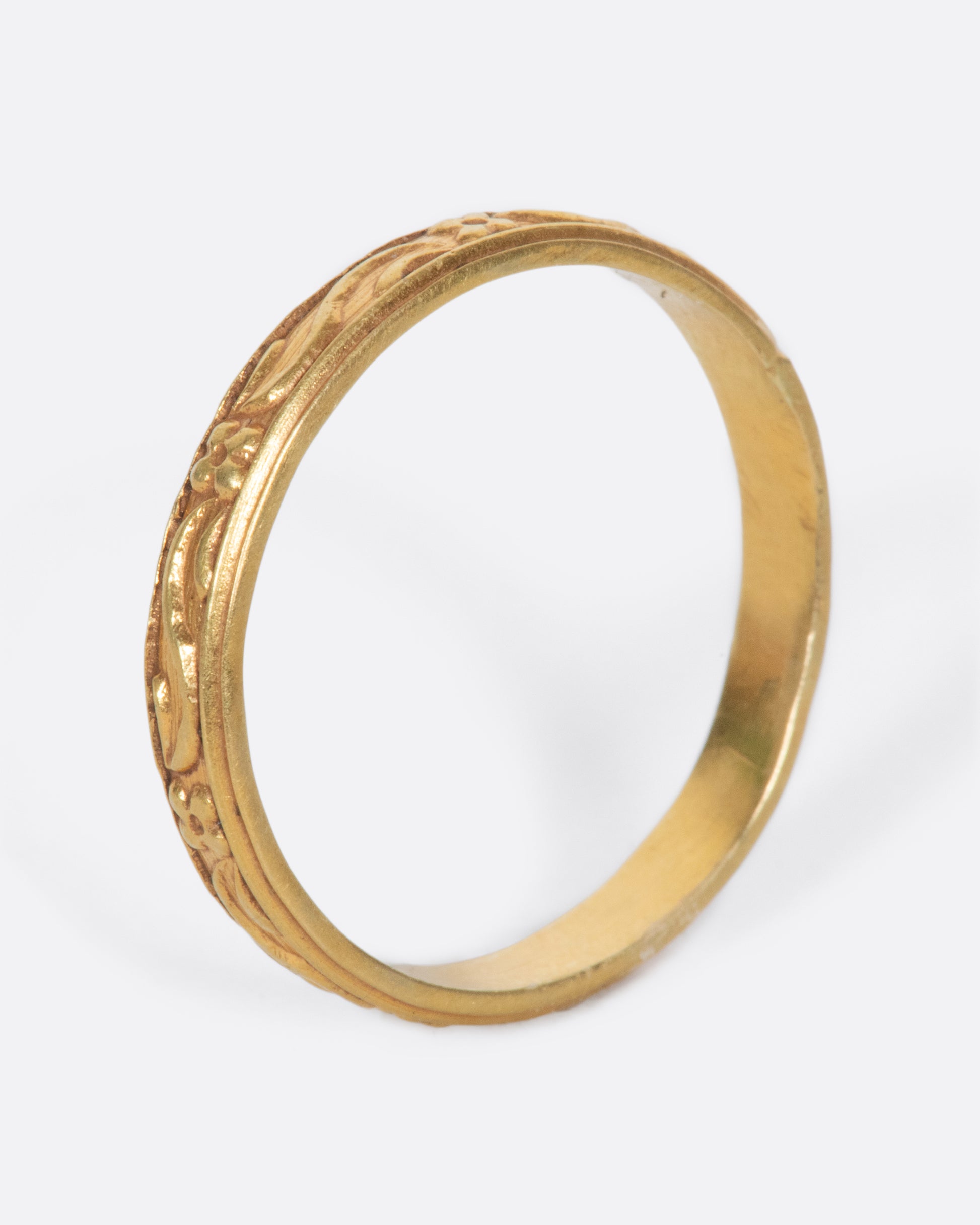 A vintage yellow gold narrow band ring with flowers and leaves throughout.