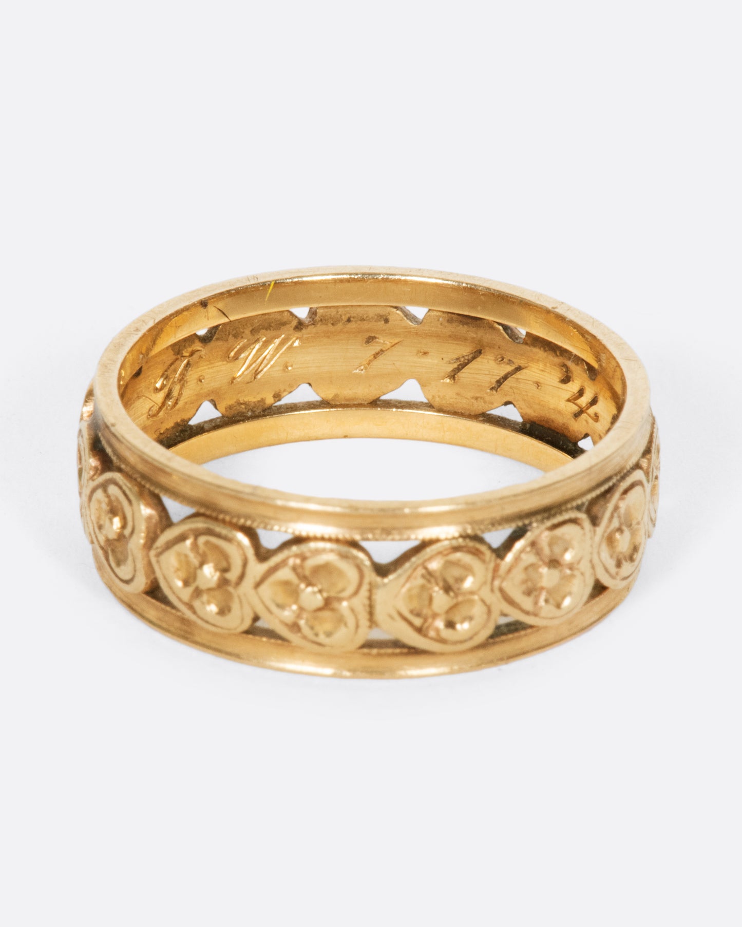 A yellow gold band ring lined with sideways hearts, shown from the side.