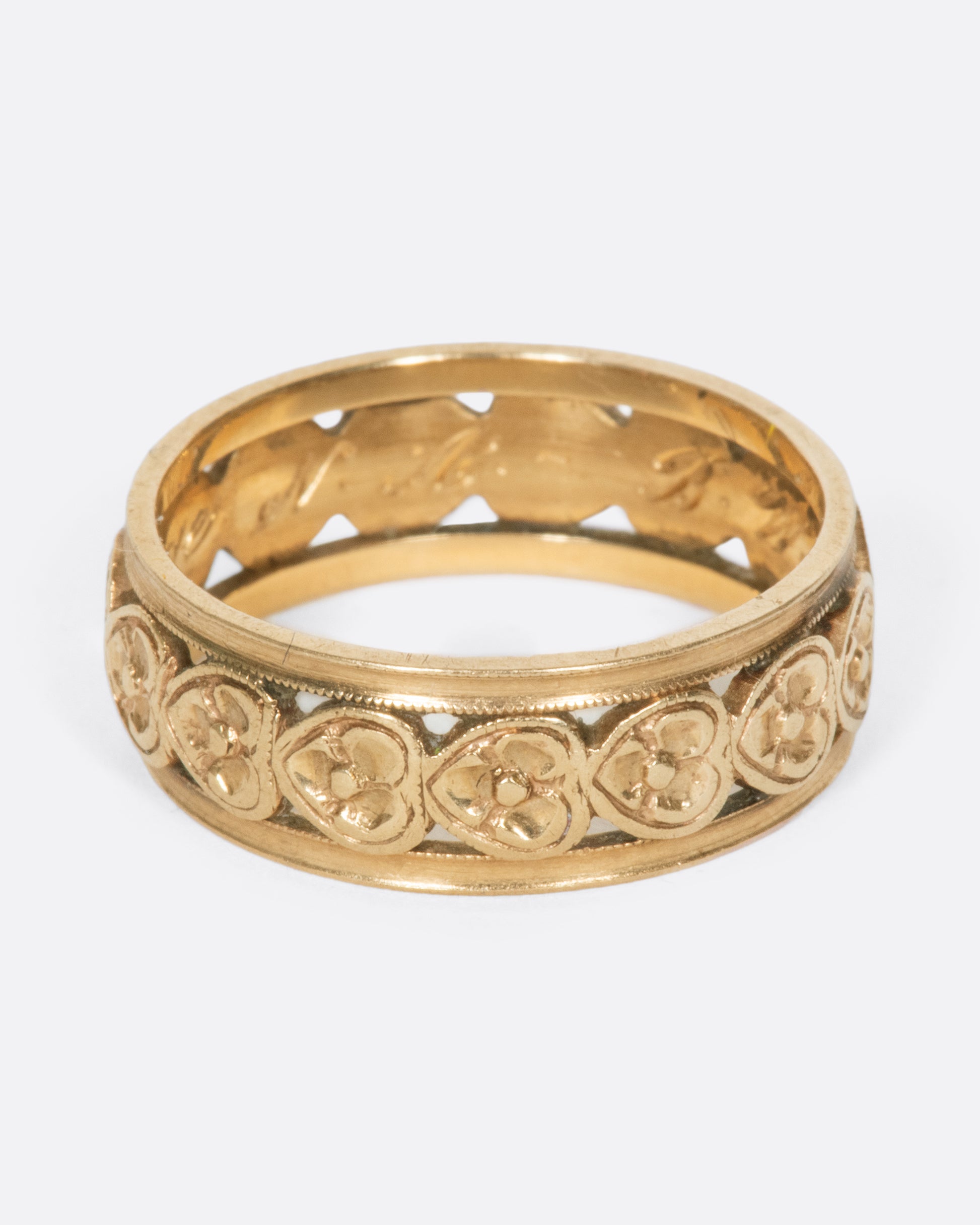 A yellow gold band ring lined with sideways hearts, shown from the side.