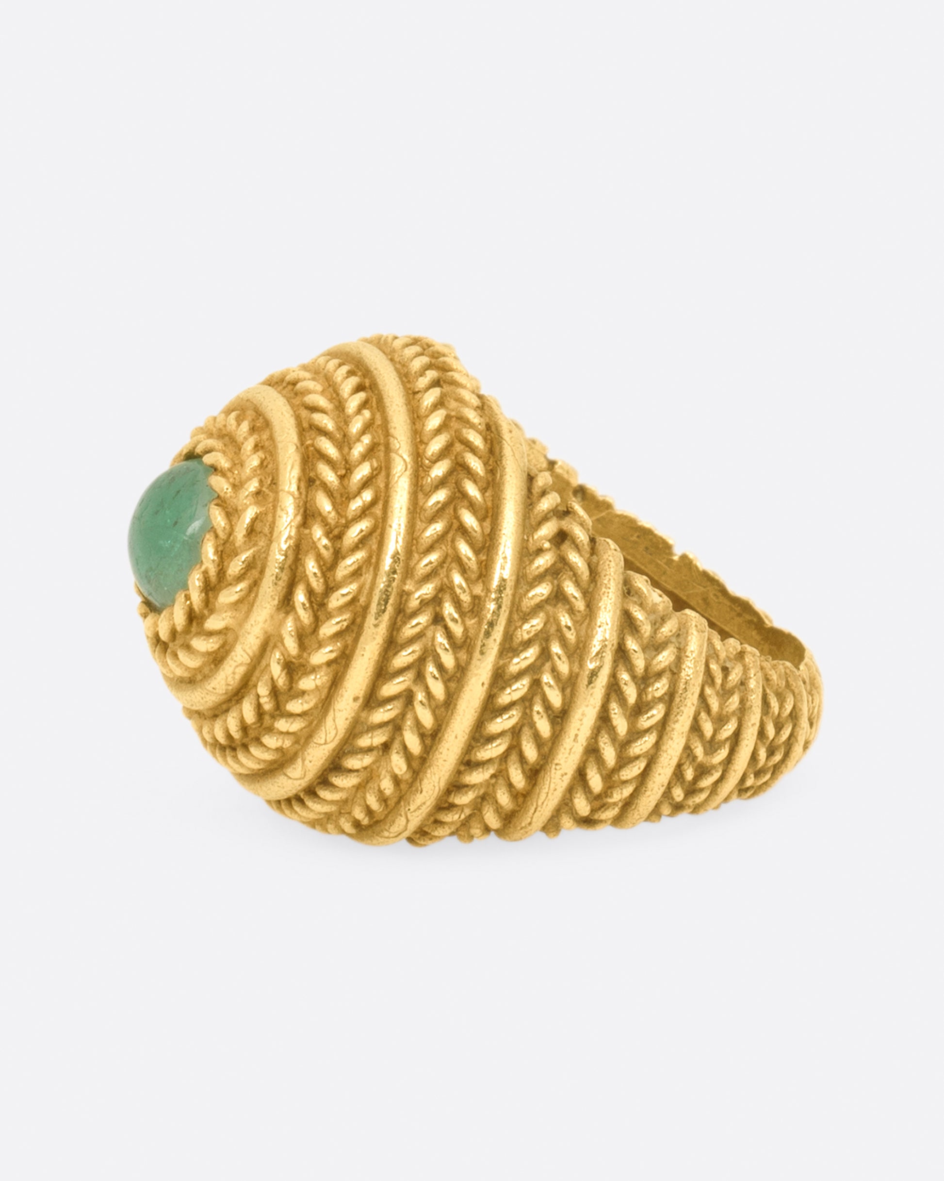 A dome ring covered in braided texture with an emerald cabochon at its peak.