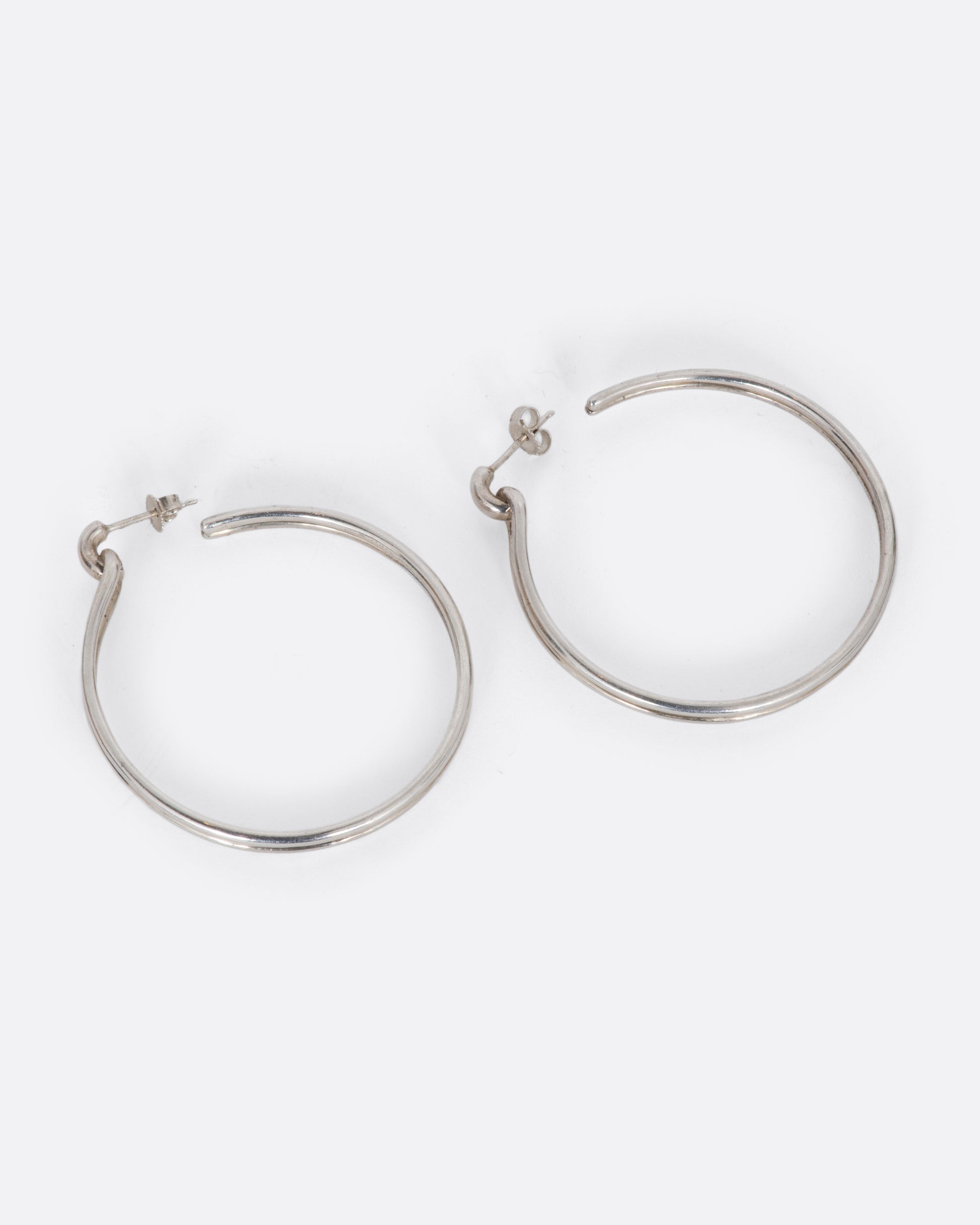 A pair of vintage sterling silver hoop earrings that connect to their posts with what looks like a loop.