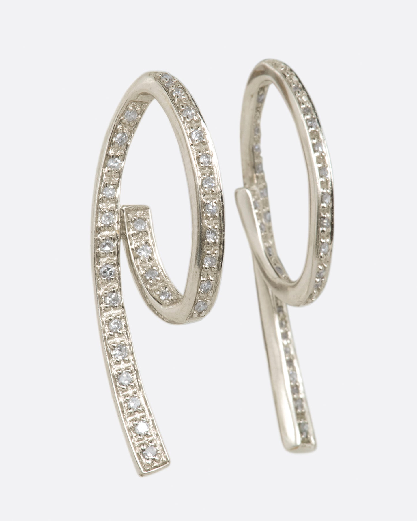 A pair of white gold, 3D loop de loop earrings, lined with diamonds. Shown from the side.