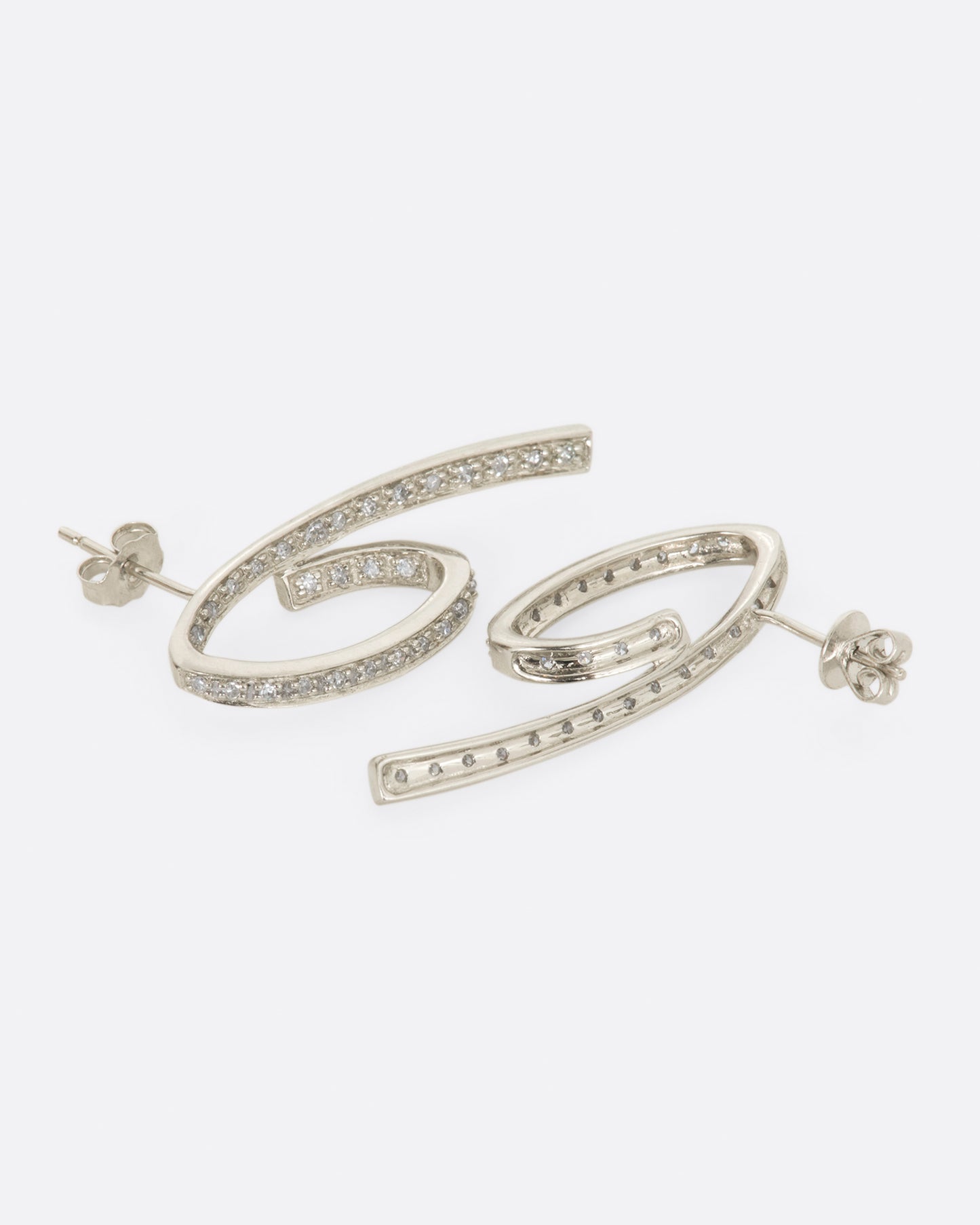 A pair of white gold, 3D loop de loop earrings, lined with diamonds. Shown from the side.