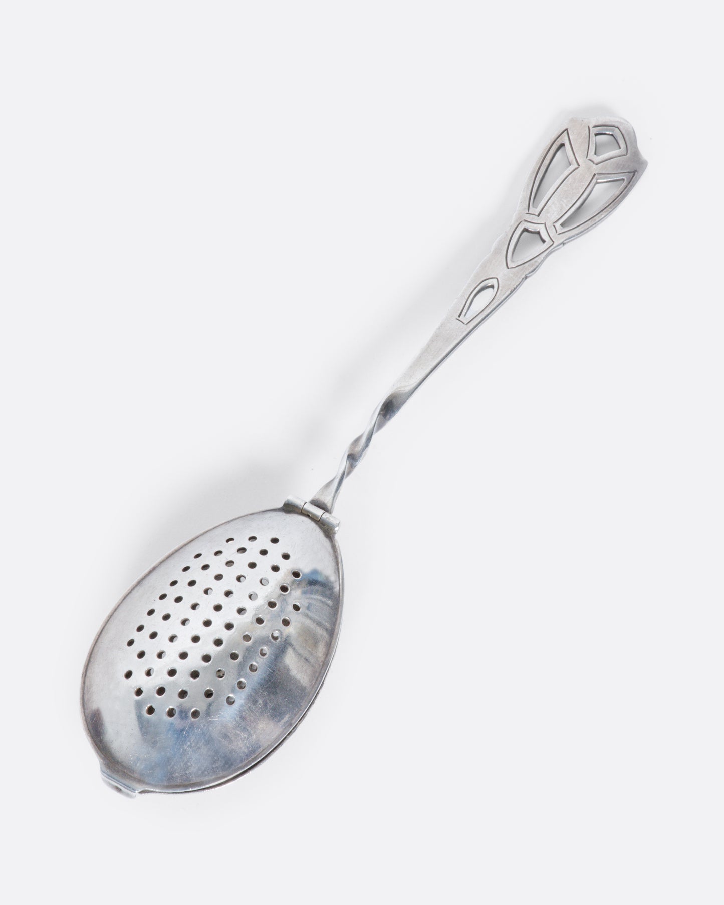 A perforated sterling silver spoon with a detailed cutout handle and a hinged perforated lid to create a tea diffuser.