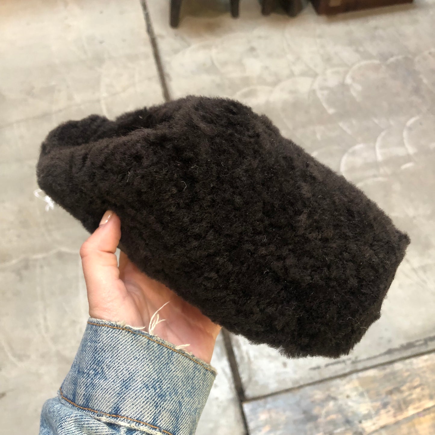 Dark brown sheepskin slipper, being held by a person from the side.